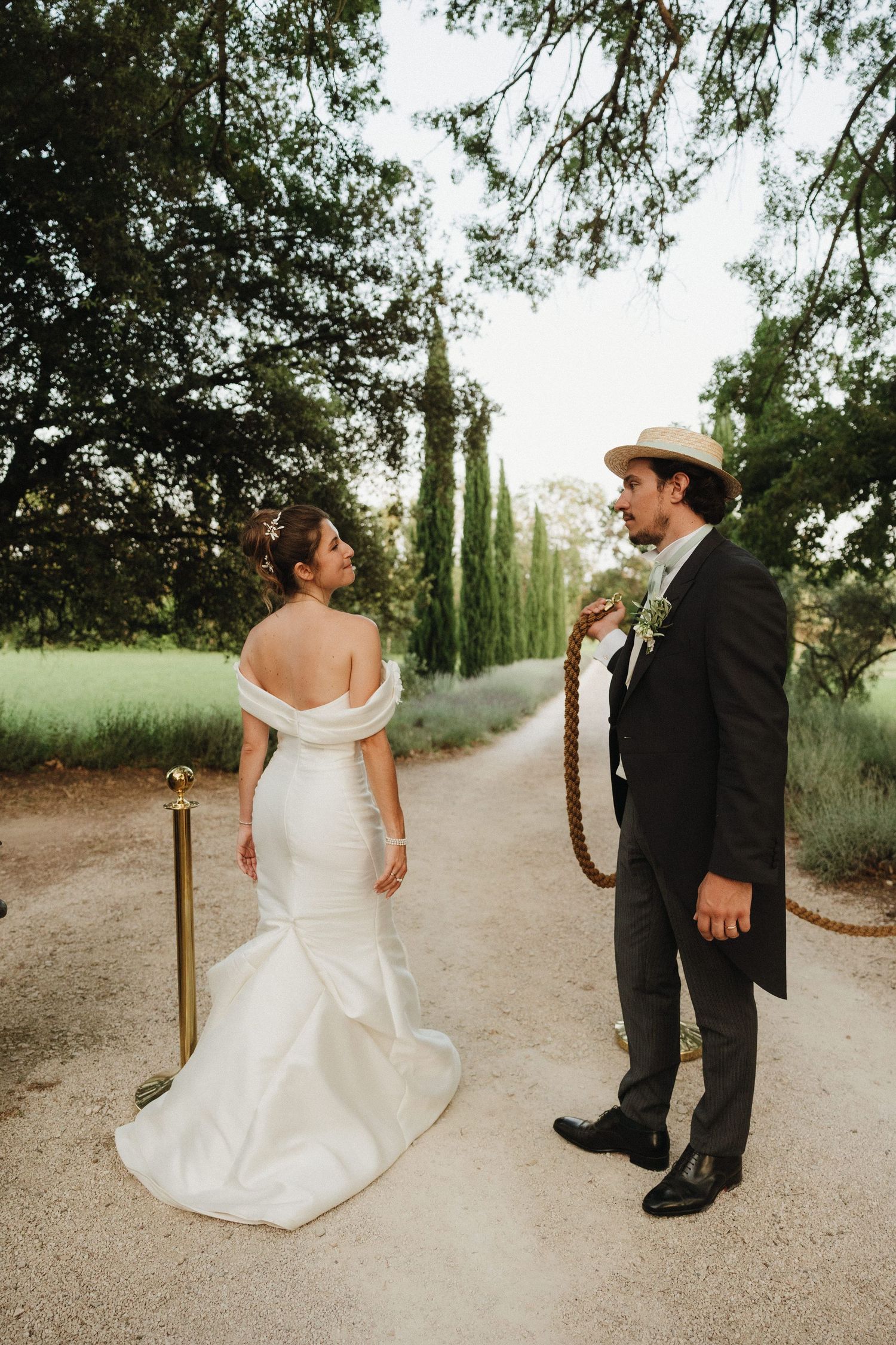 A couple sharing playful moments on a path lined with cypress trees.