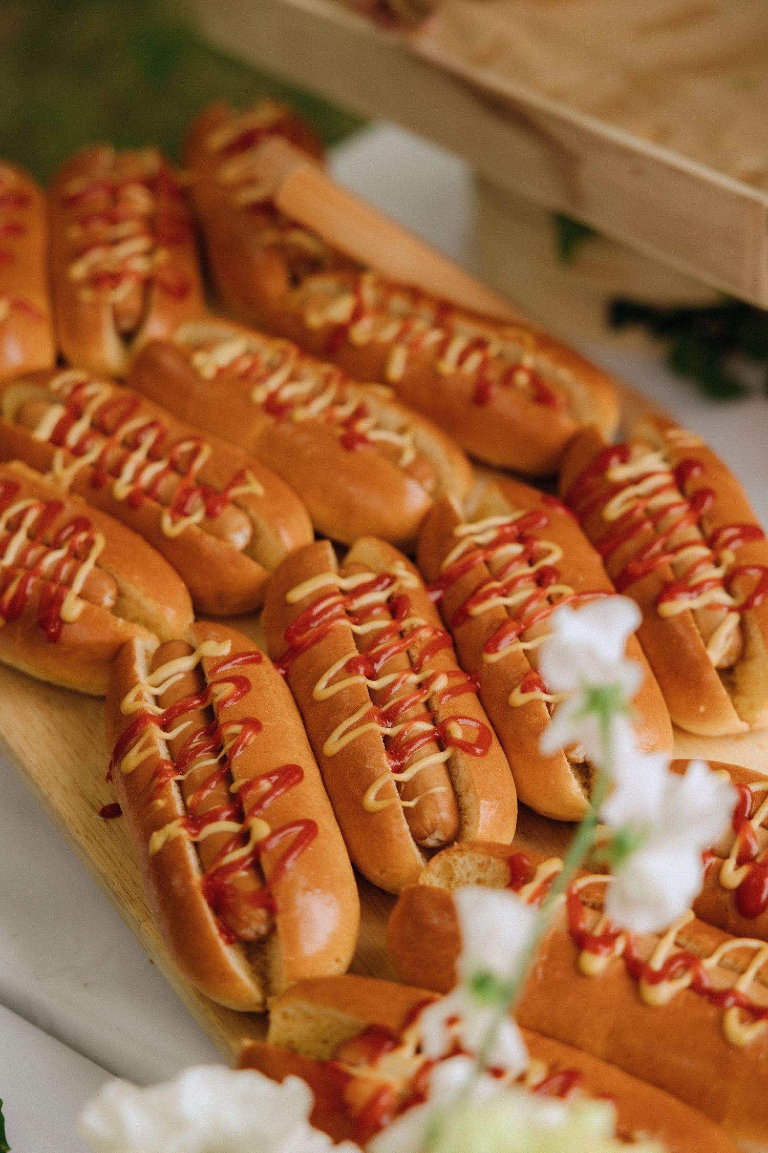 Gourmet hot dogs topped with drizzled sauce arranged in rows on a serving platter.