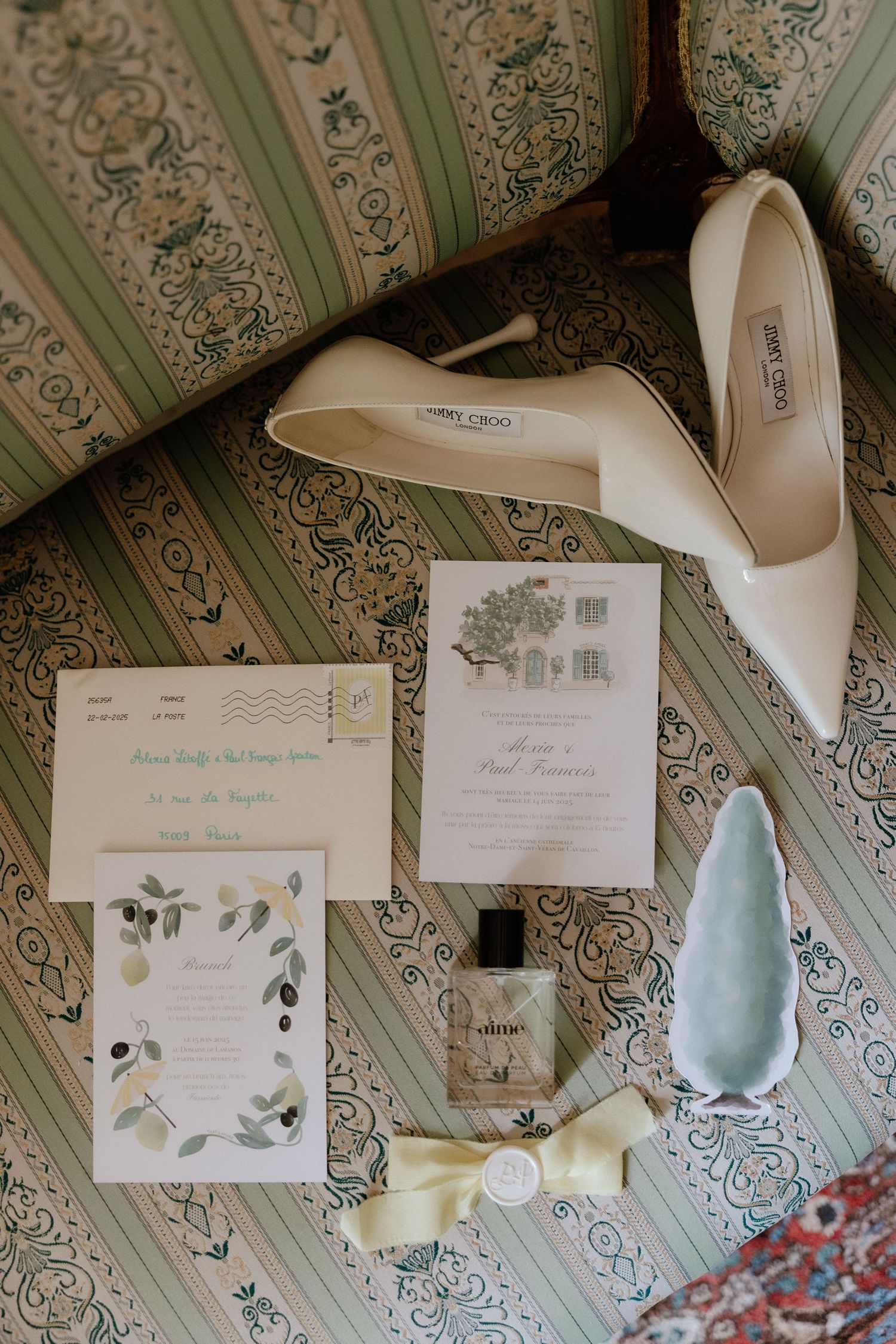 Wedding invitation suite with white heels and floral designs laid out on a vintage wallpapered surface.