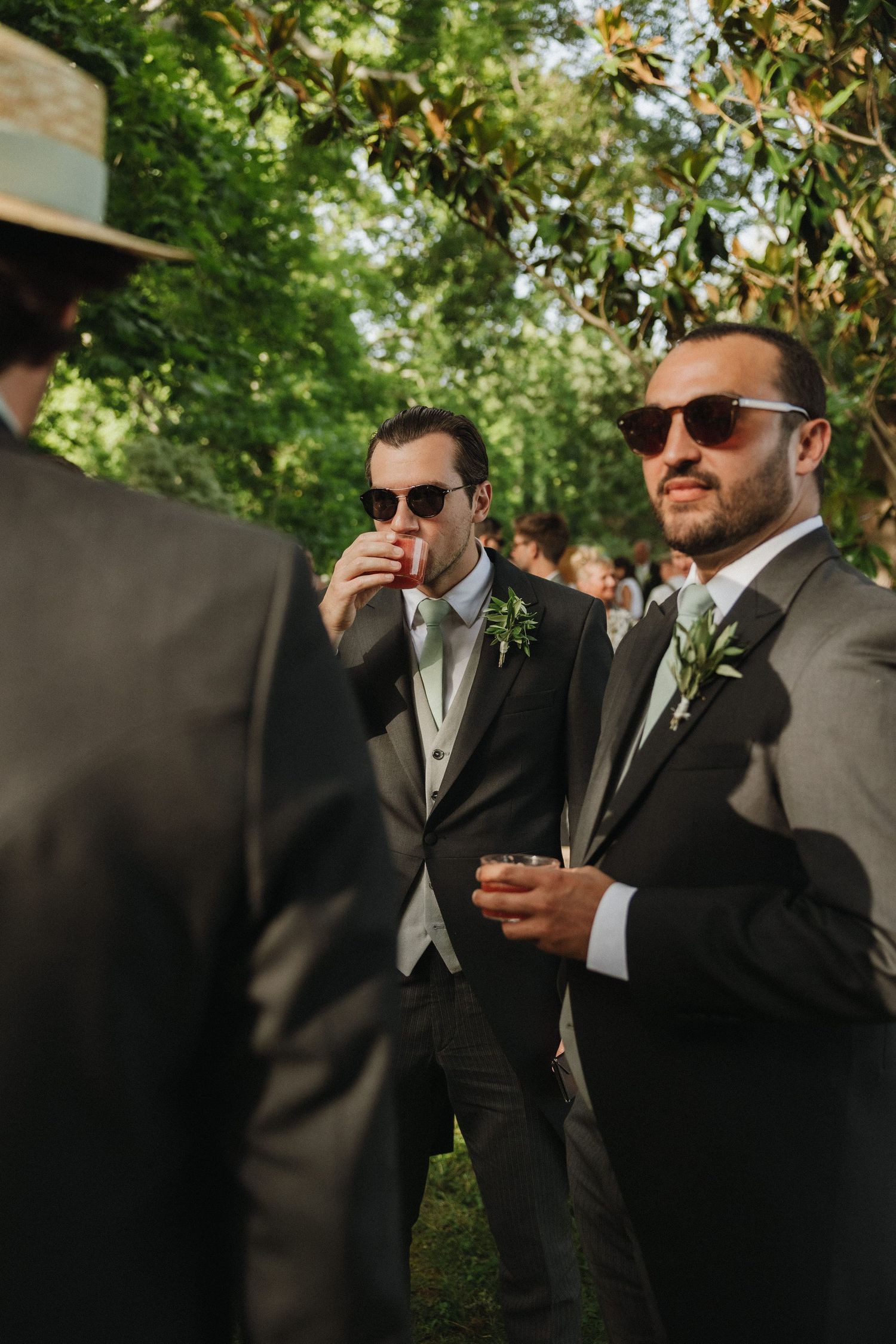 Groomsmen in formal suits and sunglasses gather outdoors.