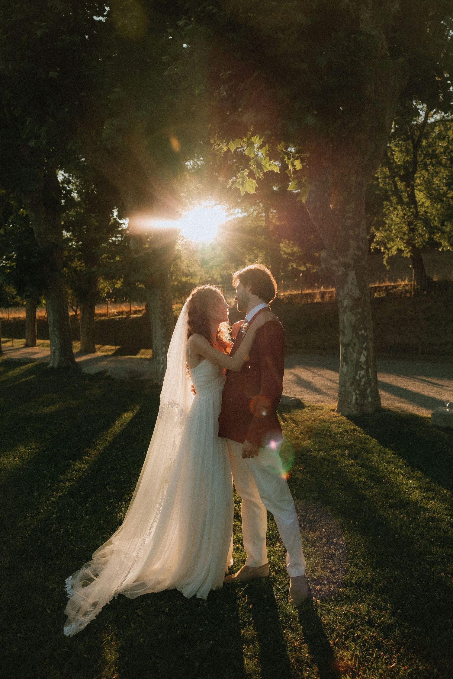 Newlyweds embrace in golden sunset light filtering through trees in an outdoor wedding setting.