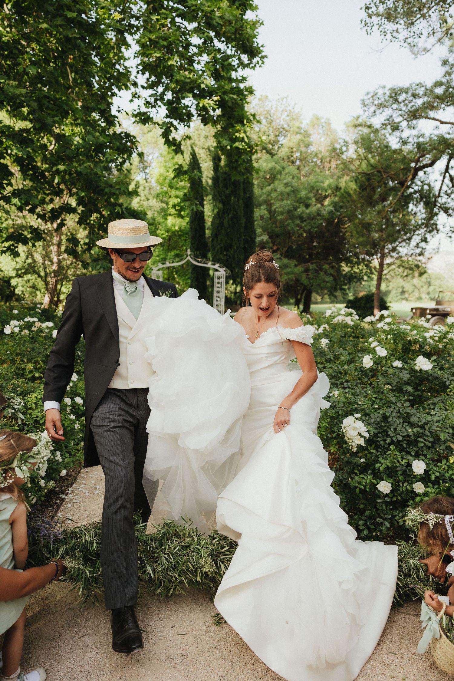 A newlywed couple walks through a garden path with flowing white wedding dress.