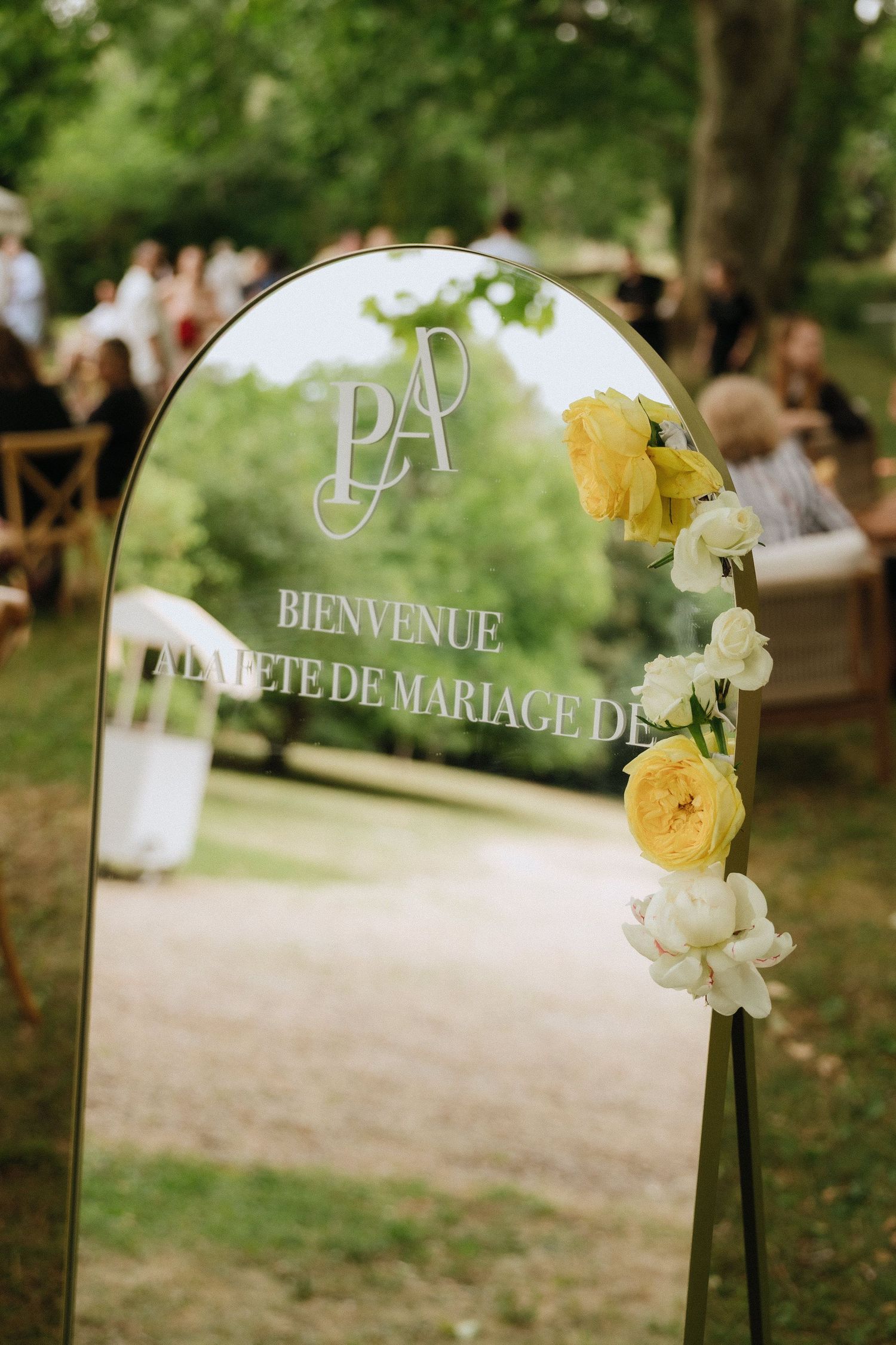 An elegant wedding welcome sign with yellow roses and white flowers in an arched frame.