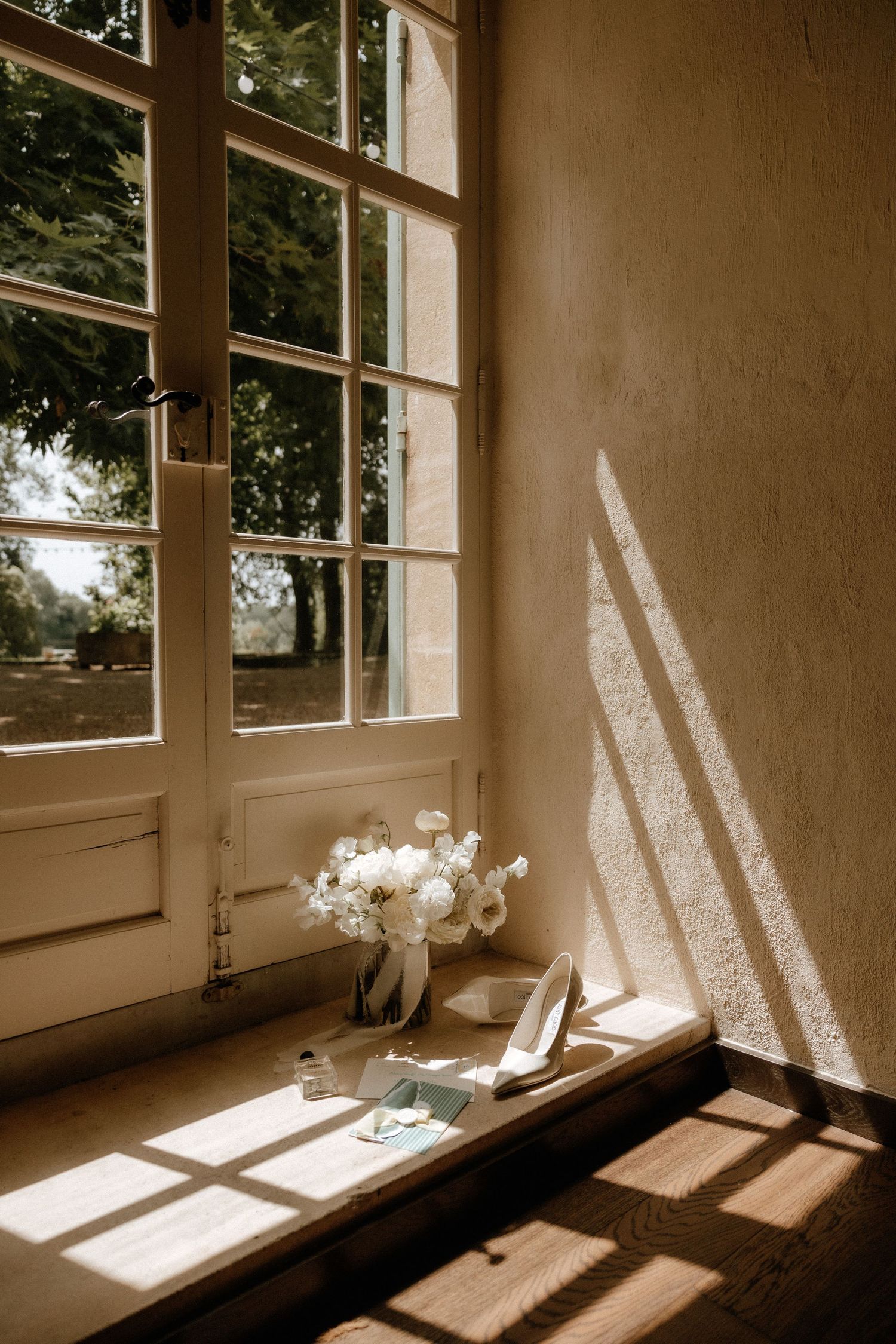 Sunlight streams through windows casting dramatic shadows on a windowsill with a small vase of flowers in sepia tones.