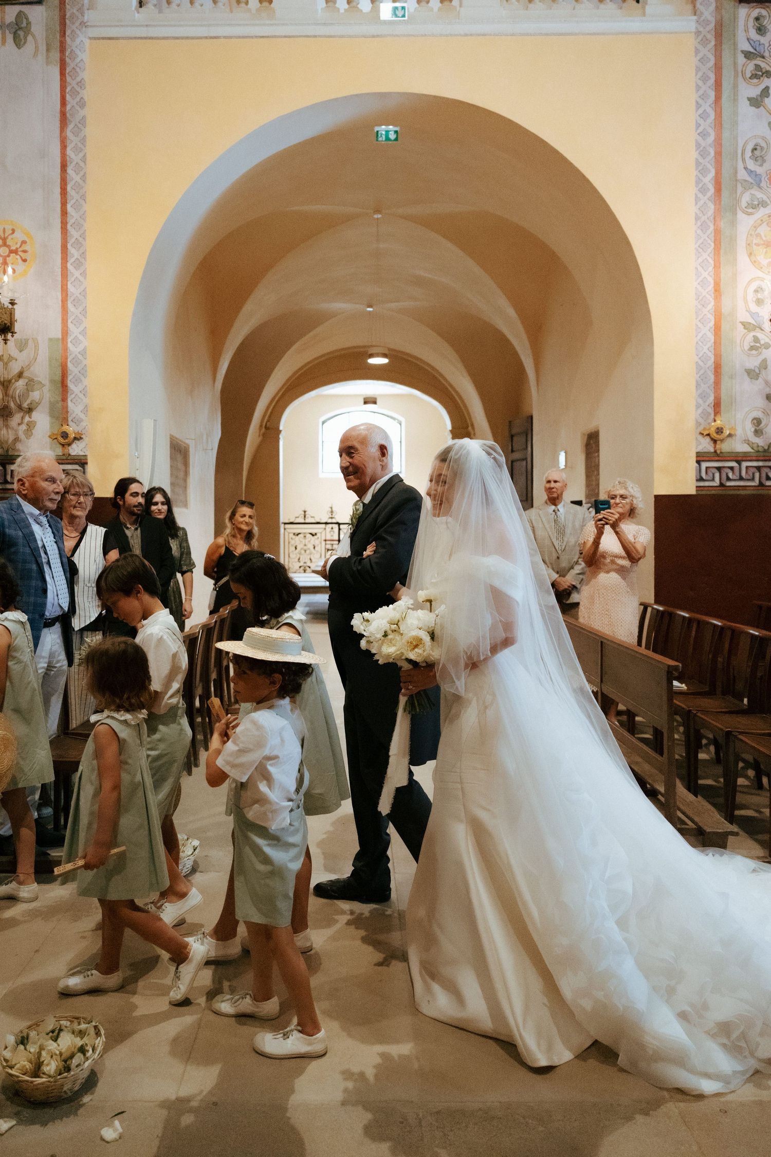 Wedding ceremony processional in an ornate church with children and guests in attendance.