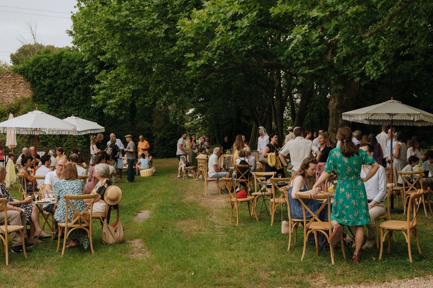 Outdoor garden wedding reception with guests seated at scattered tables under trees.