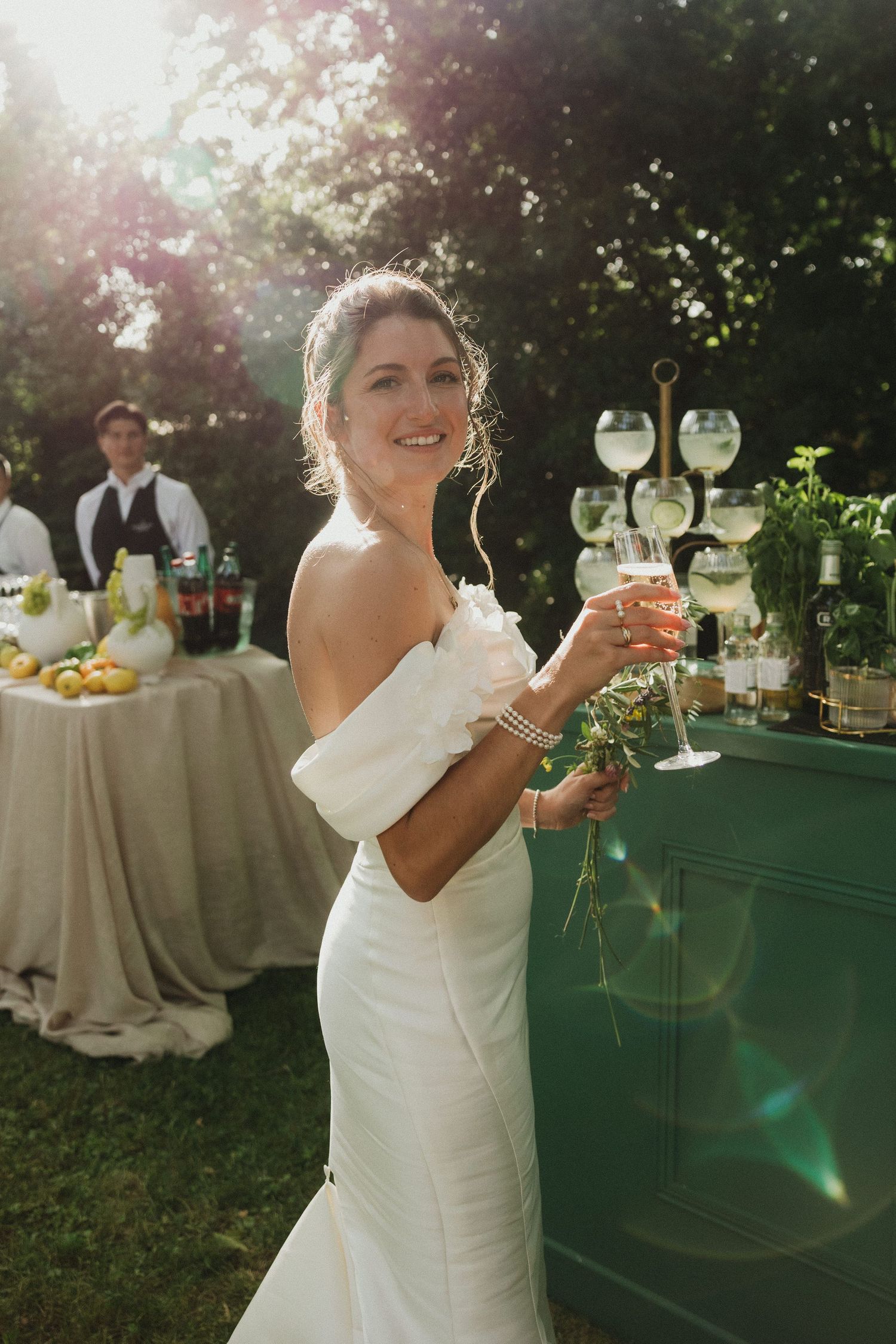 Elegant outdoor wedding reception setup with drinks and glassware on a green table.