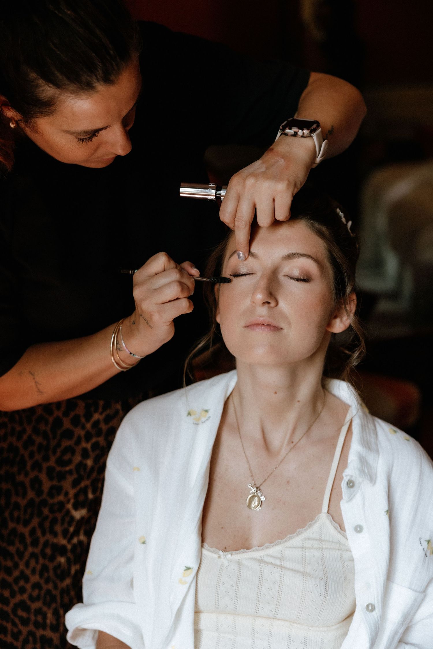 A makeup artist applies cosmetics to a client wearing white during a professional beauty session.