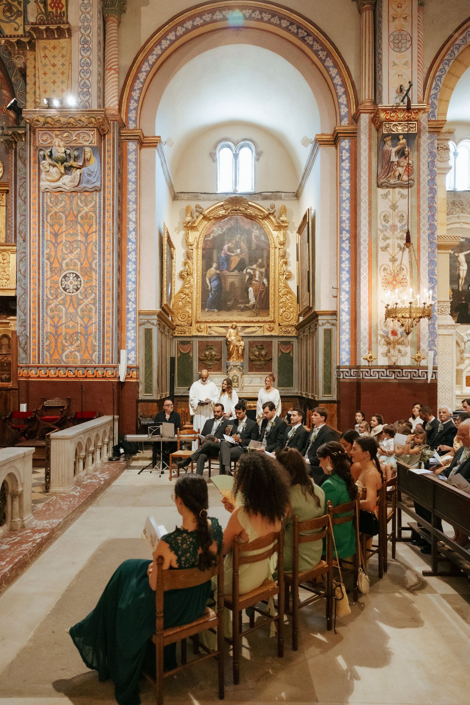 Interior of a beautifully decorated church with ornate frescoes and guests seated in pews.