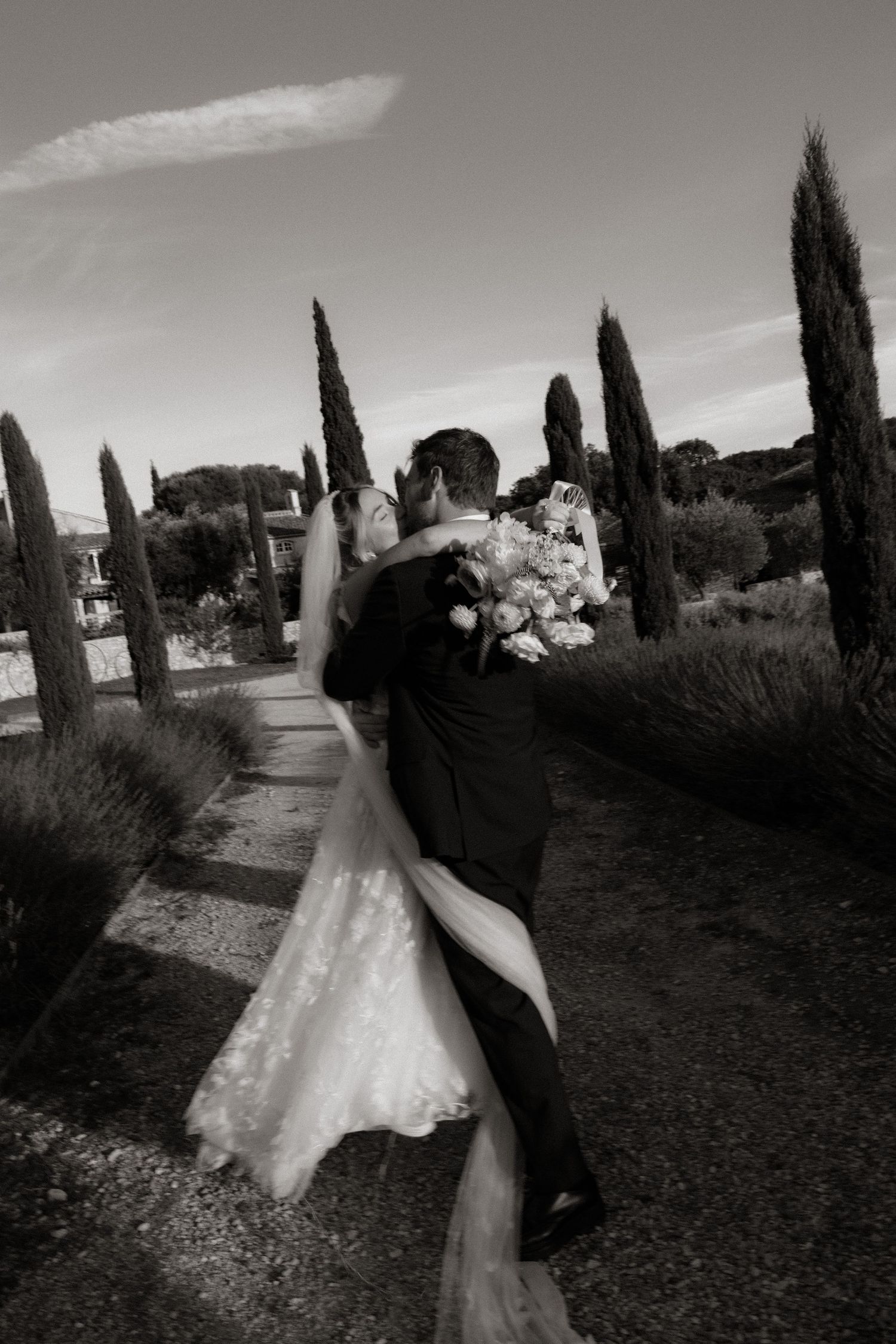 Black and white wedding photography along a cypress tree-lined path in a romantic Tuscan garden setting.