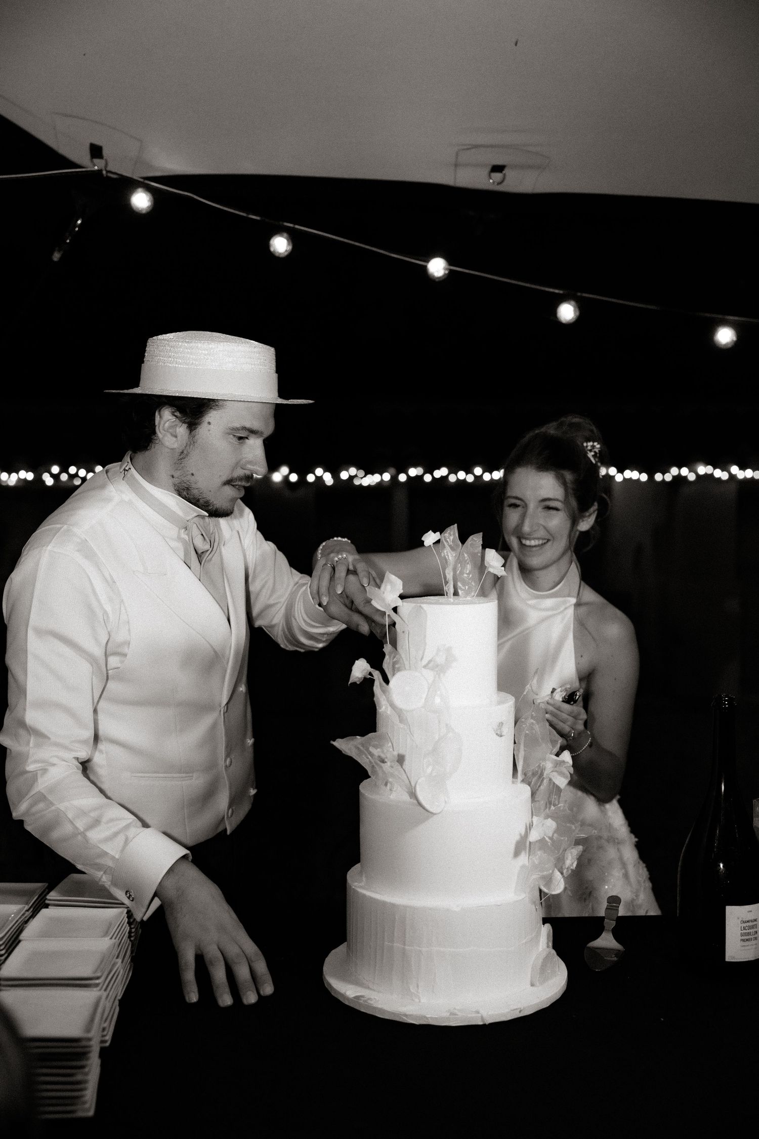 Black and white photos of wedding cake cutting with string lights in background.