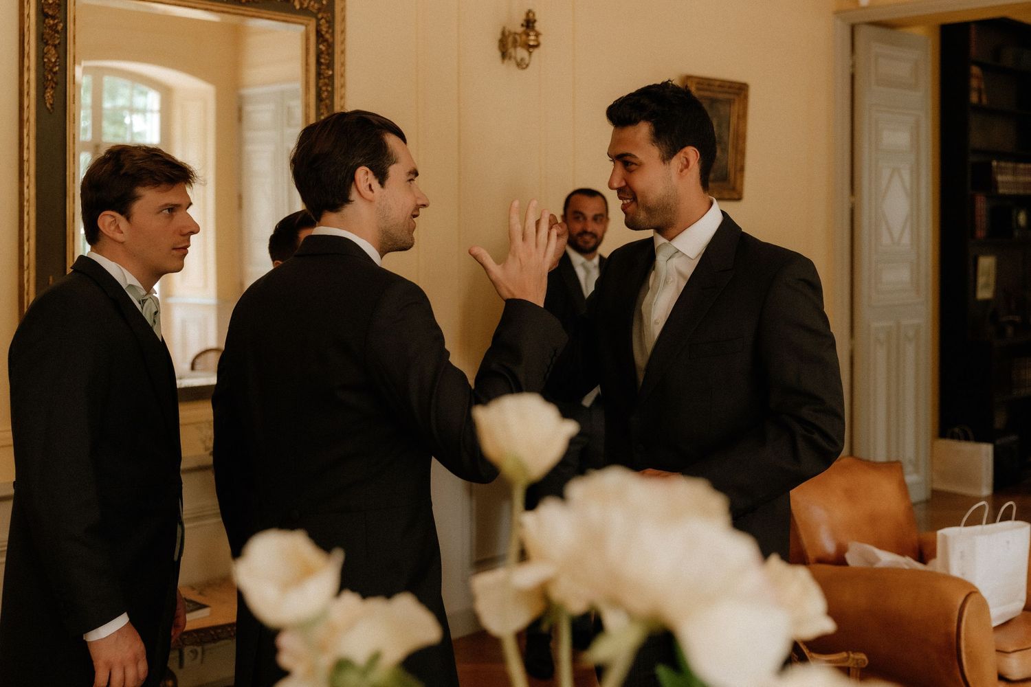 A group in formal attire gathers at an elegant indoor event with white floral arrangements.