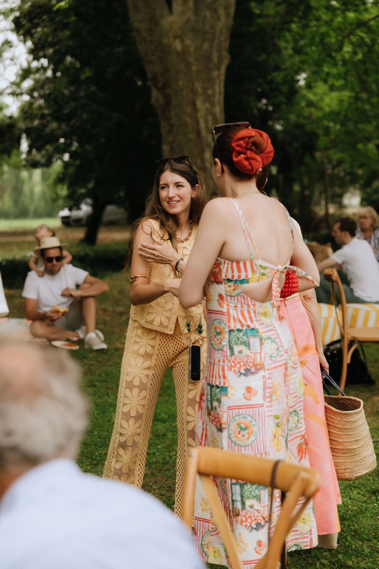 Wedding guests in colorful summer dresses socializing at an outdoor garden party.