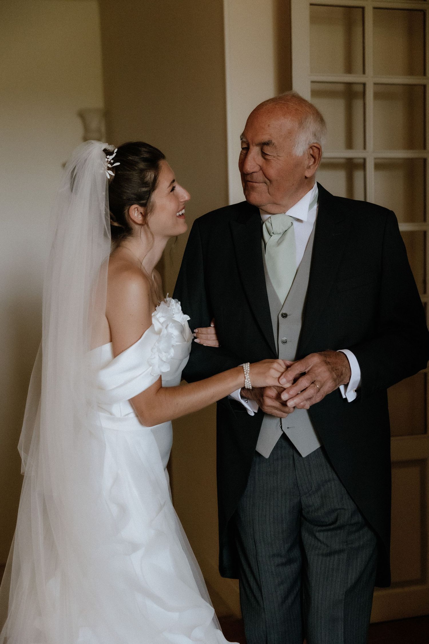 A bride in white dress dances with an older gentleman in formal attire during a wedding celebration.