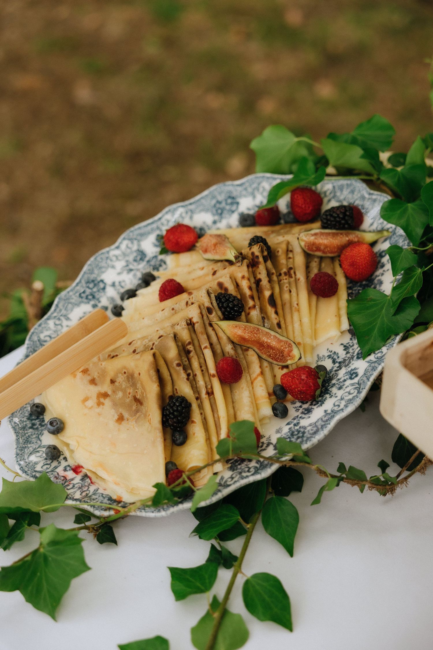 Crepes garnished with fresh berries and mint leaves served on an ornate blue and white floral plate.