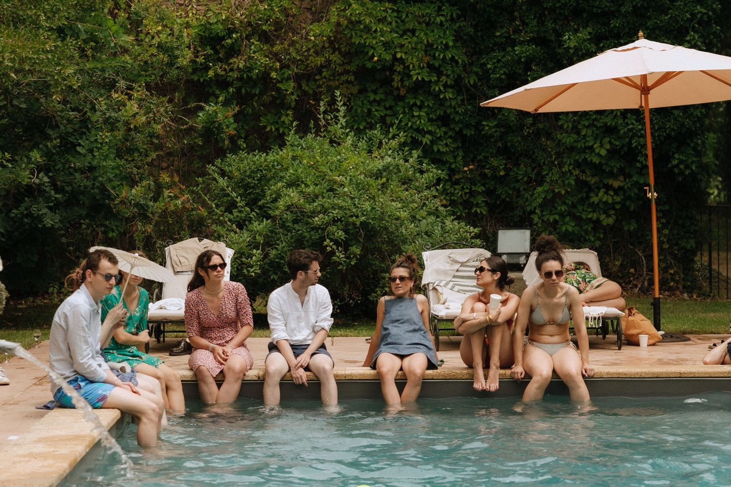 Wedding guests relaxing with feet in the pool during a casual outdoor celebration.