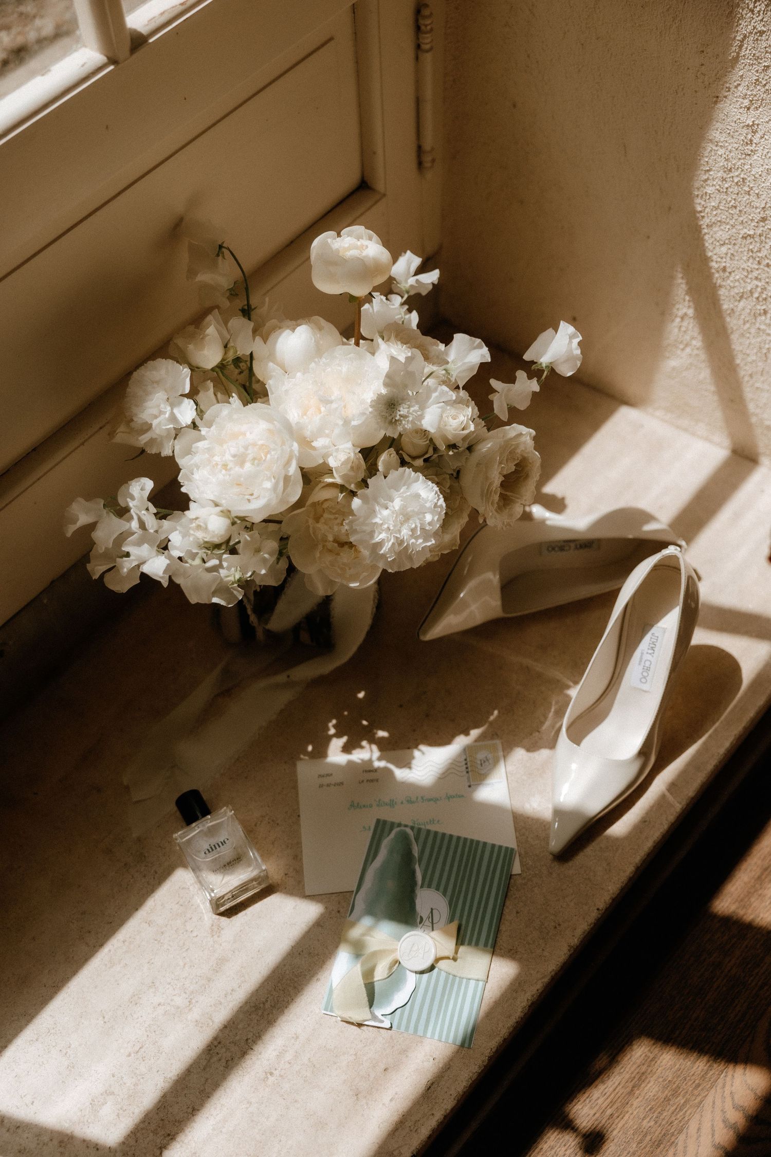 White floral bouquet, bridal shoe, and wedding accessories arranged in soft window light.