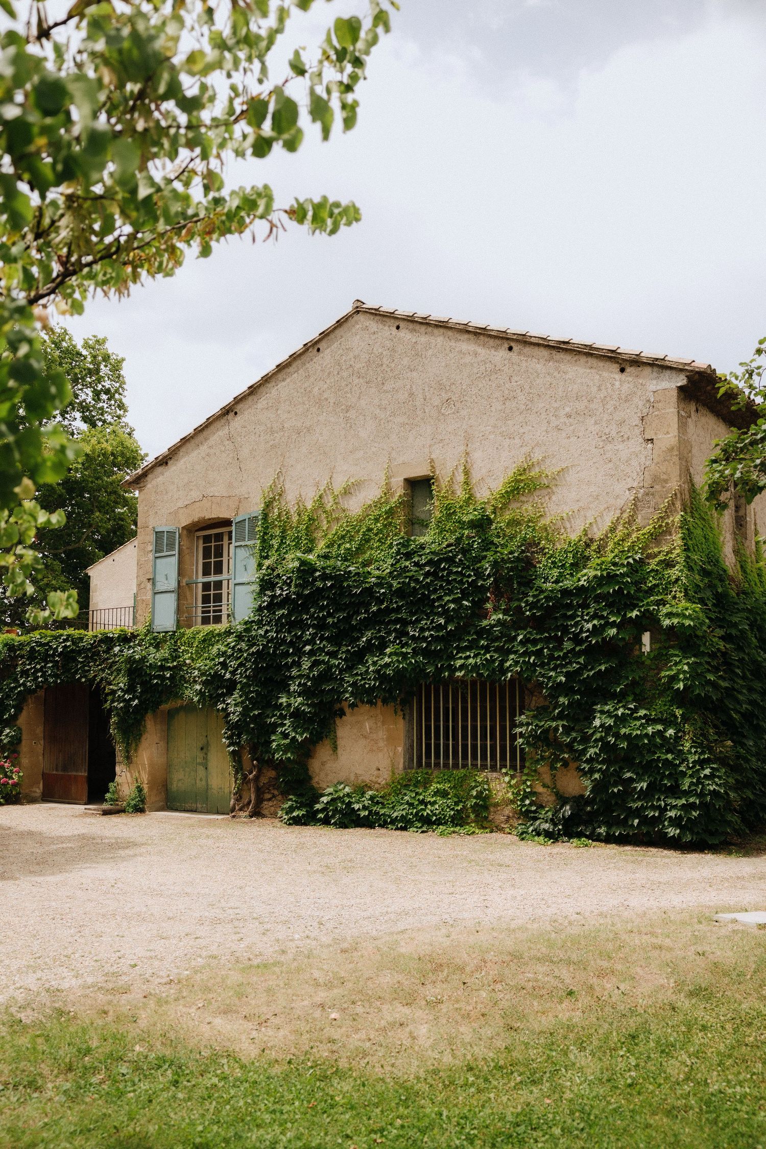 Rustic stone buildings with ivy covered walls and gravel driveway in countryside setting.