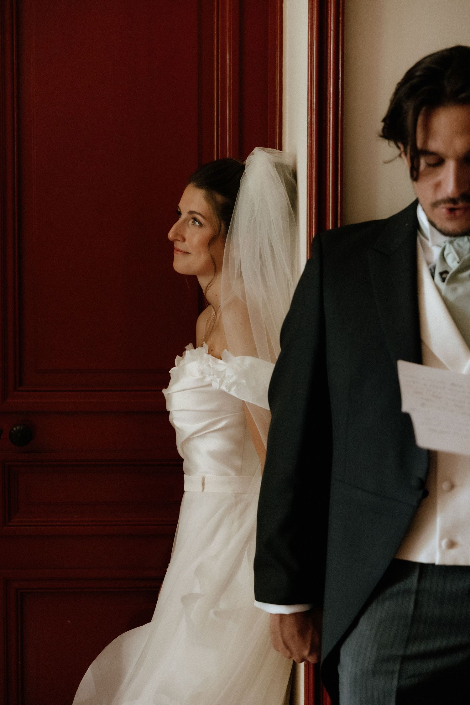 Artistic black and white portrait of couple in formal wedding attire against dark wood paneled wall.