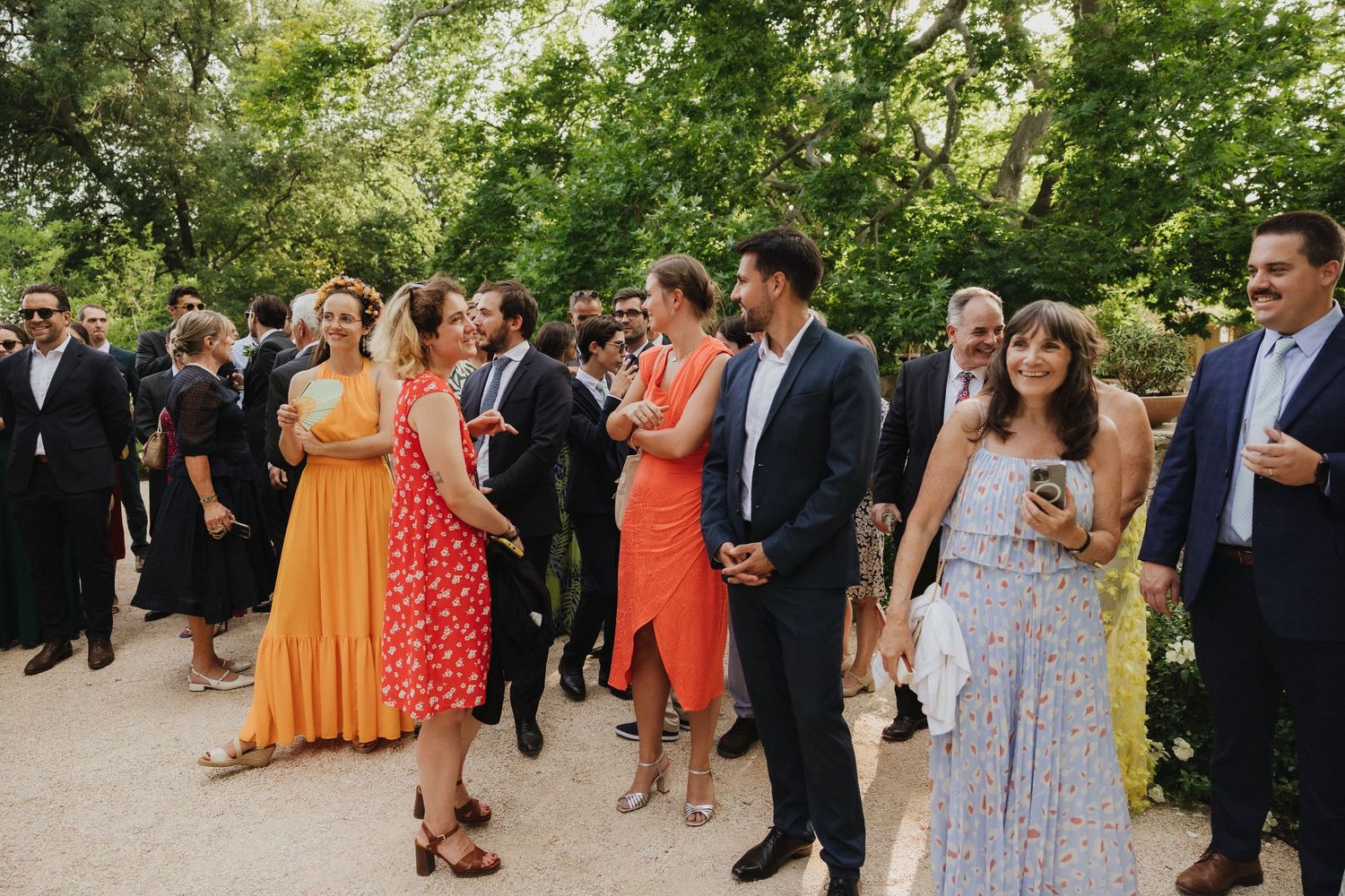 Wedding guests in colorful summer attire gathering outdoors during a celebration.