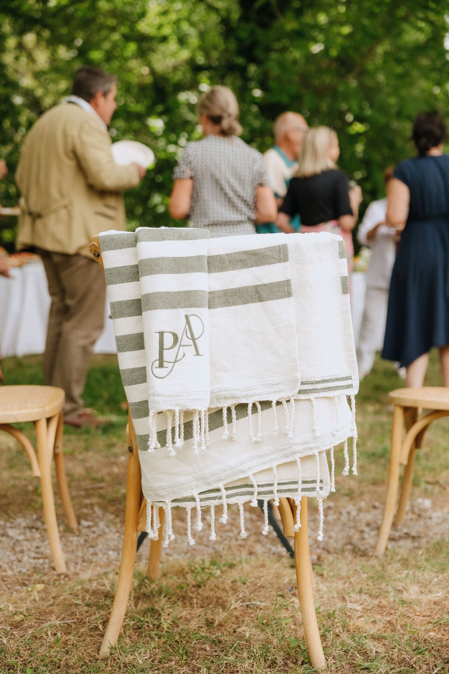 Striped monogrammed throw blanket draped over wooden chair at outdoor gathering.