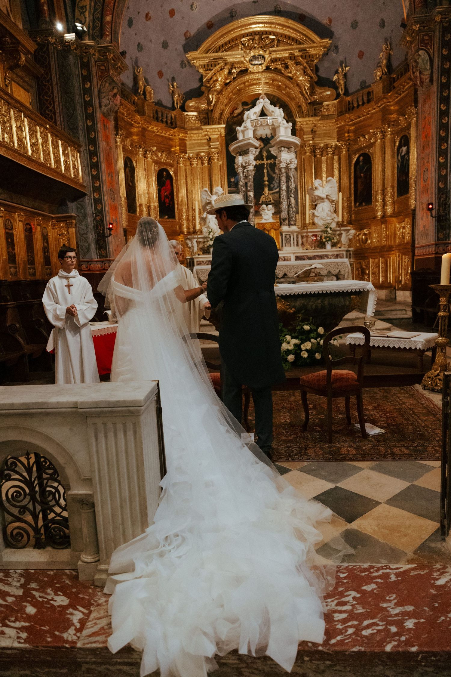 Ornate church interior with golden baroque details and marble floors during a wedding ceremony.