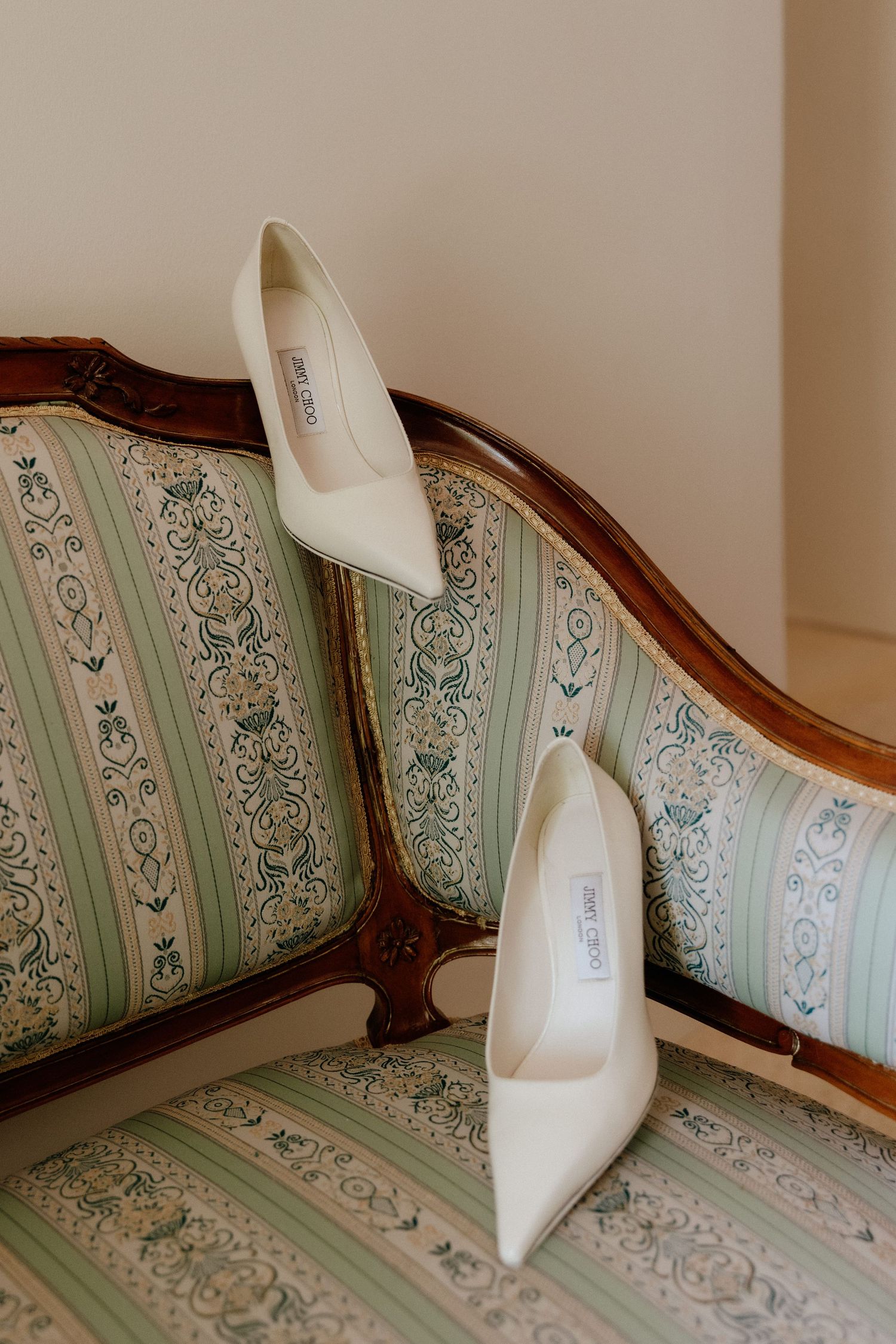 White bridal heels placed on a vintage couch with mint green and floral upholstery pattern.