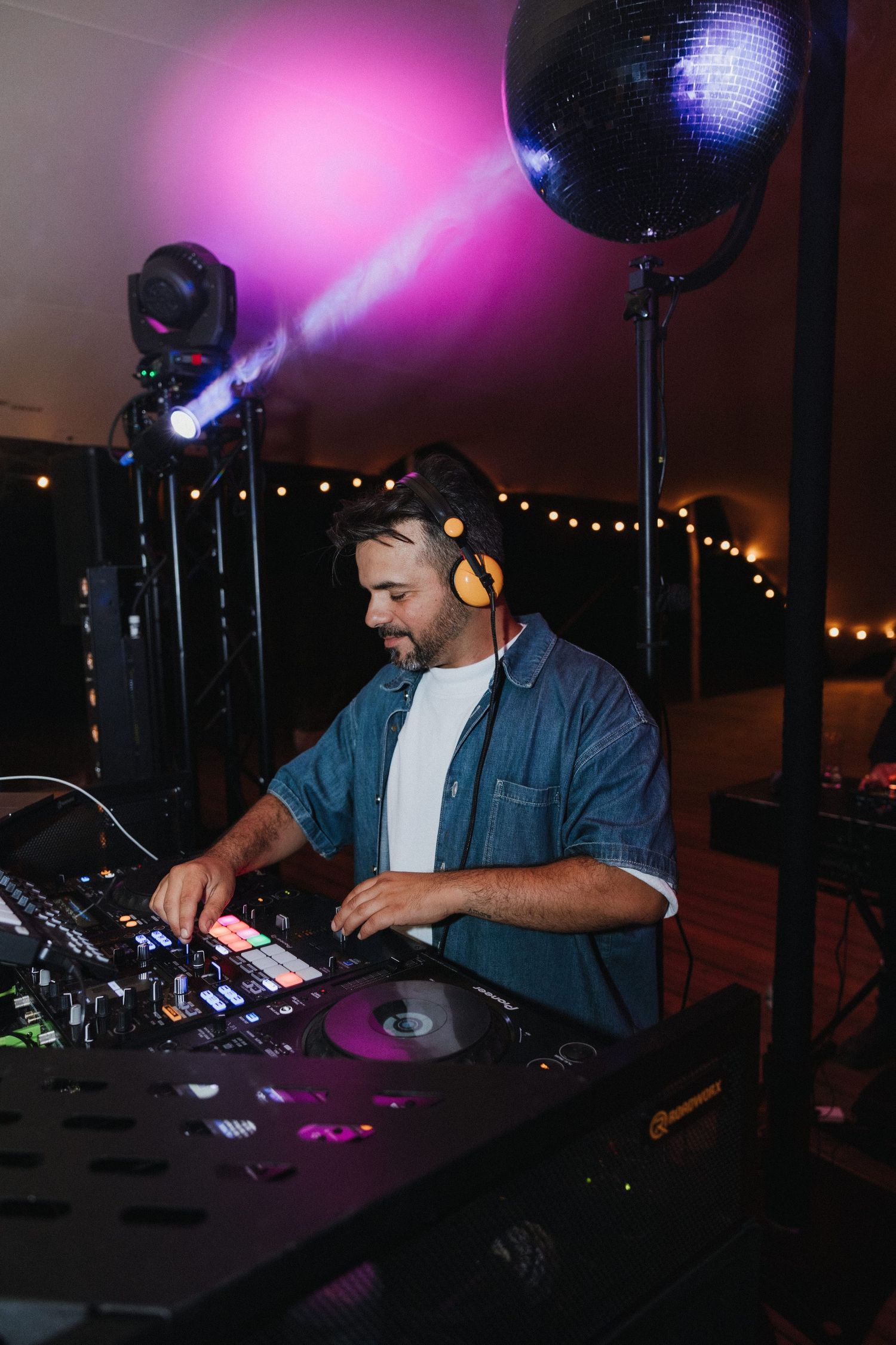 DJ performs at wedding reception with disco ball and purple lighting effects.