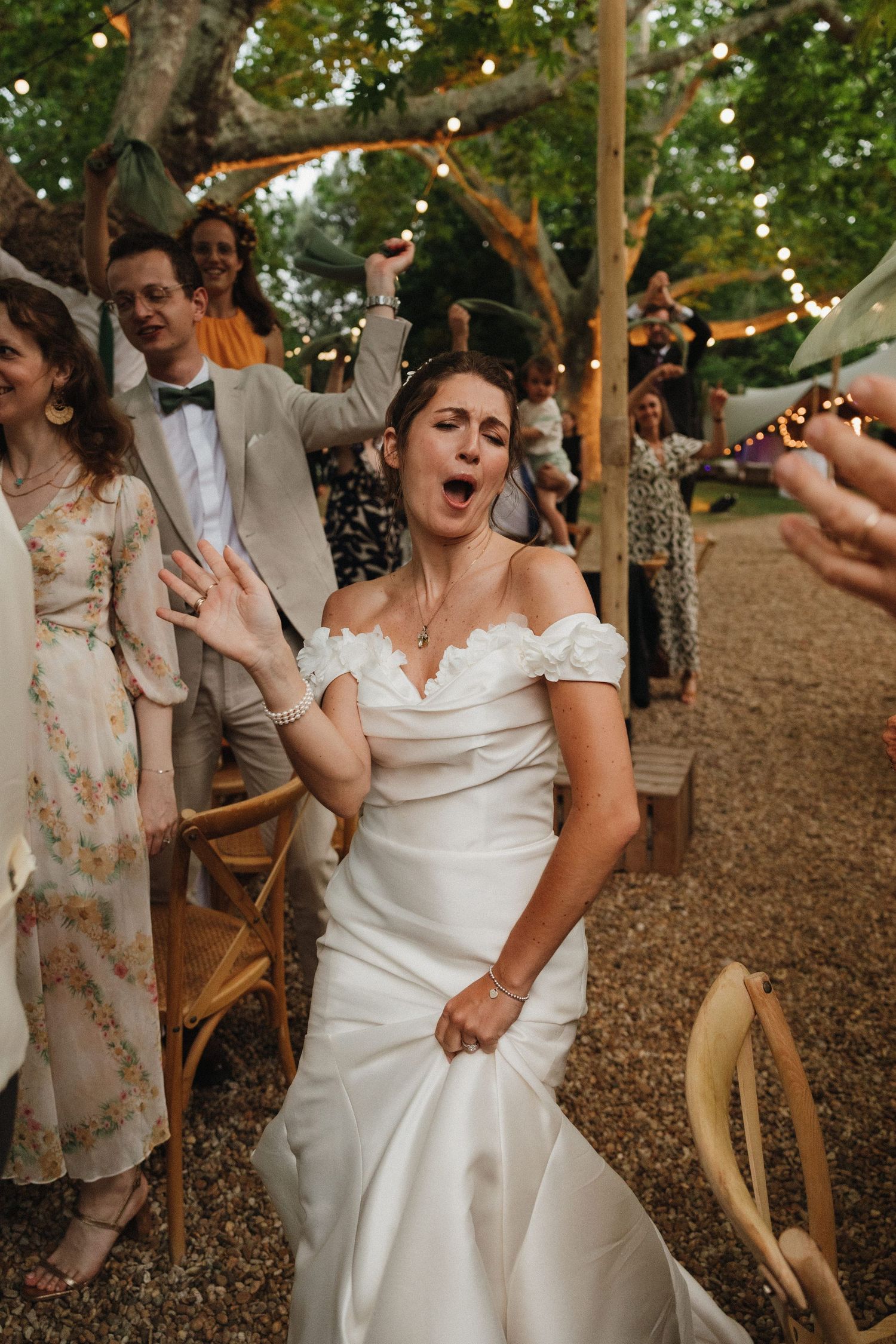 Wedding guests dancing and celebrating at an outdoor reception under string lights.