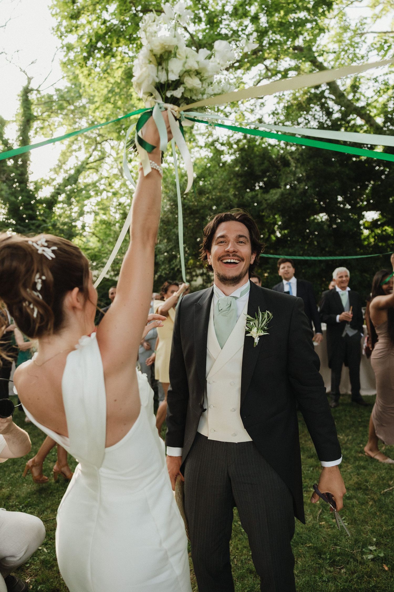 Joyful wedding celebration moment as bride holds up bouquet during outdoor garden party.