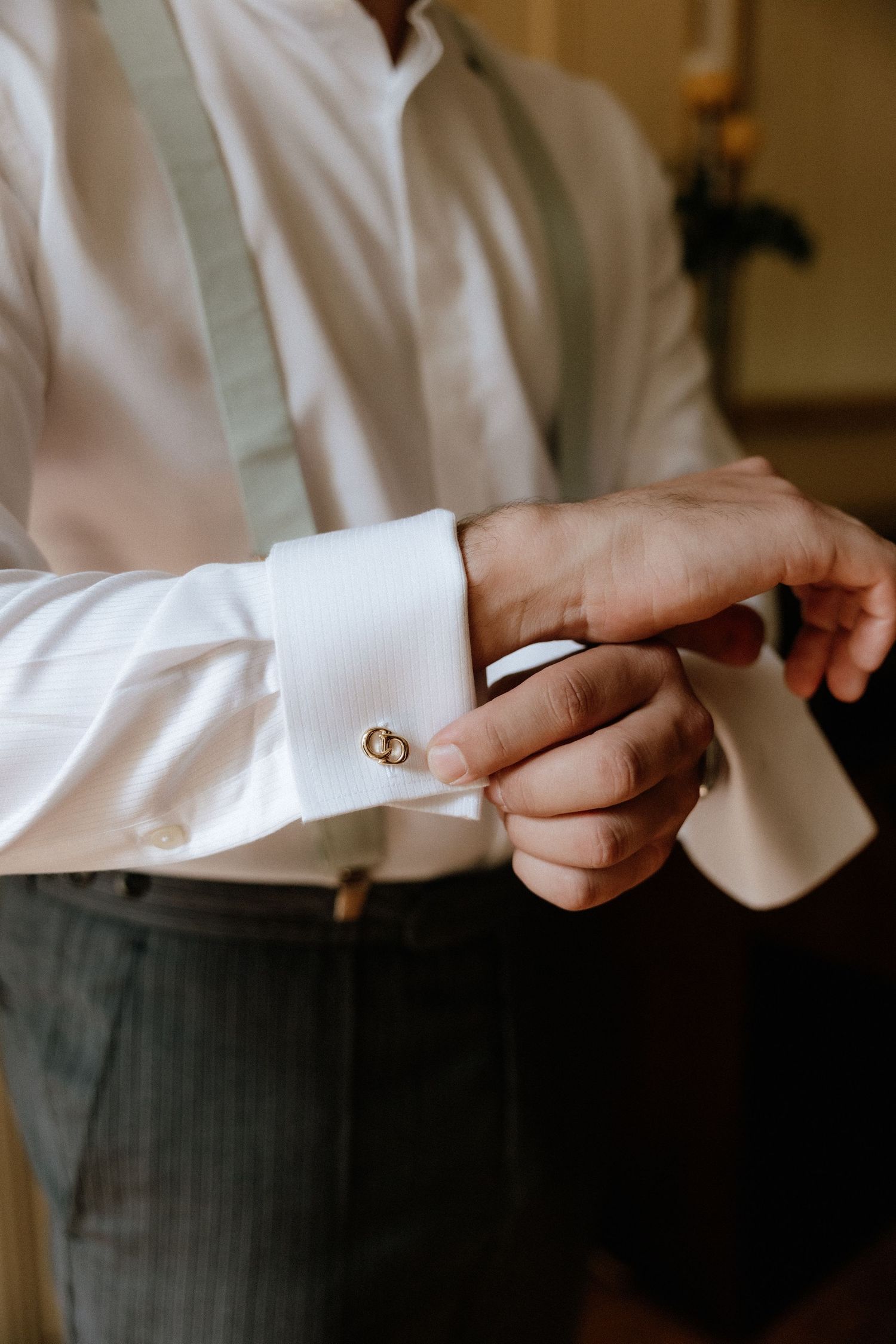 Close-up of hands adjusting a white shirt cuff with suspenders visible in formal attire.