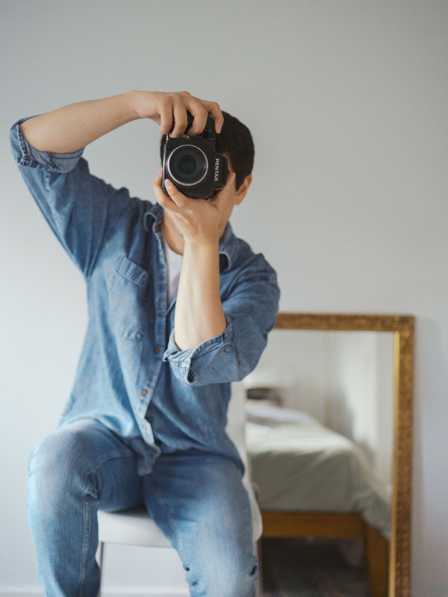 Pacific Northwest photographer capturing a self-portrait at home with a Pentax 645N medium format film camera, wearing a denim outfit