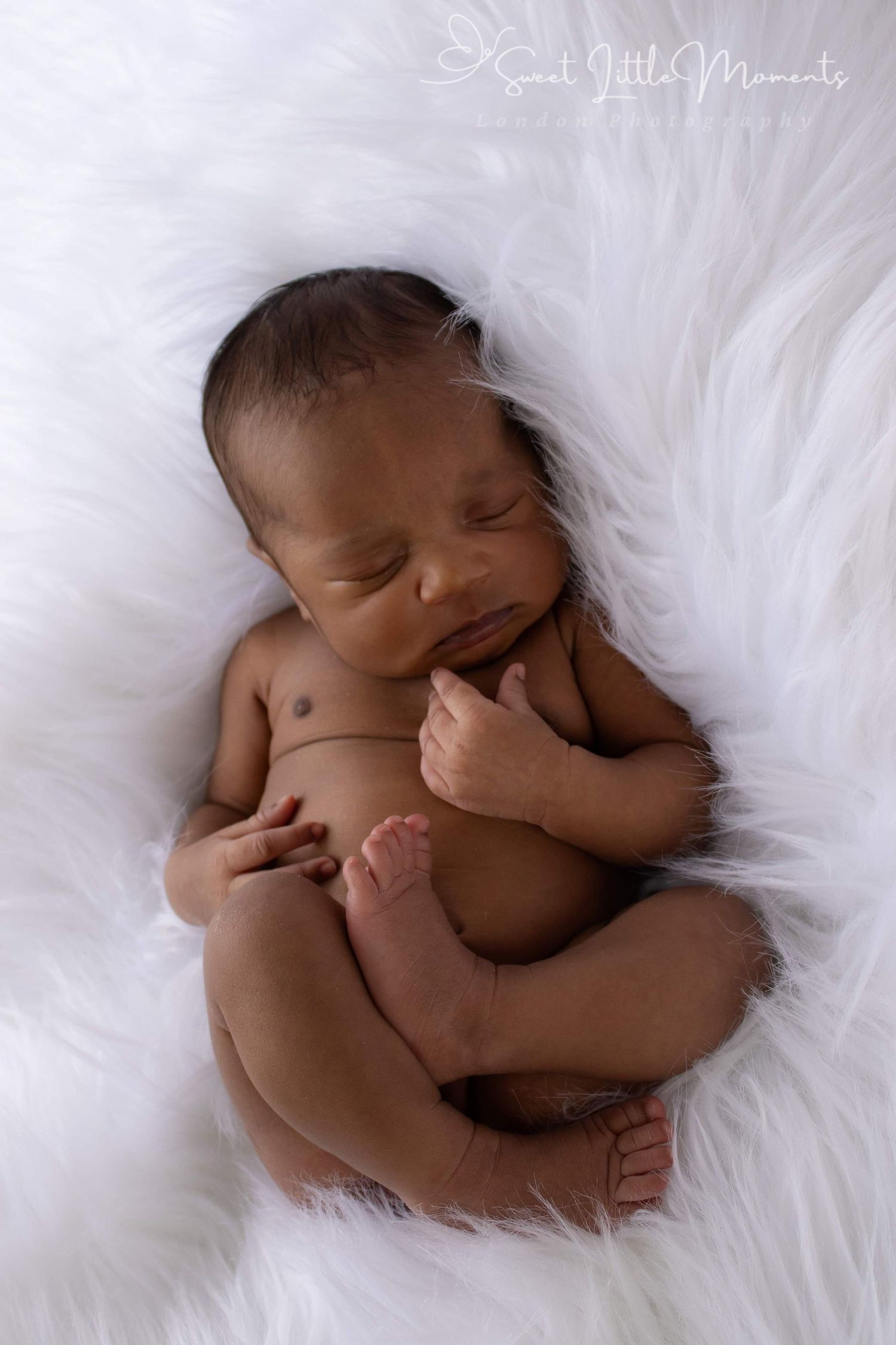 Sleeping newborn curled up peacefully on white fluffy blanket during studio photo session.