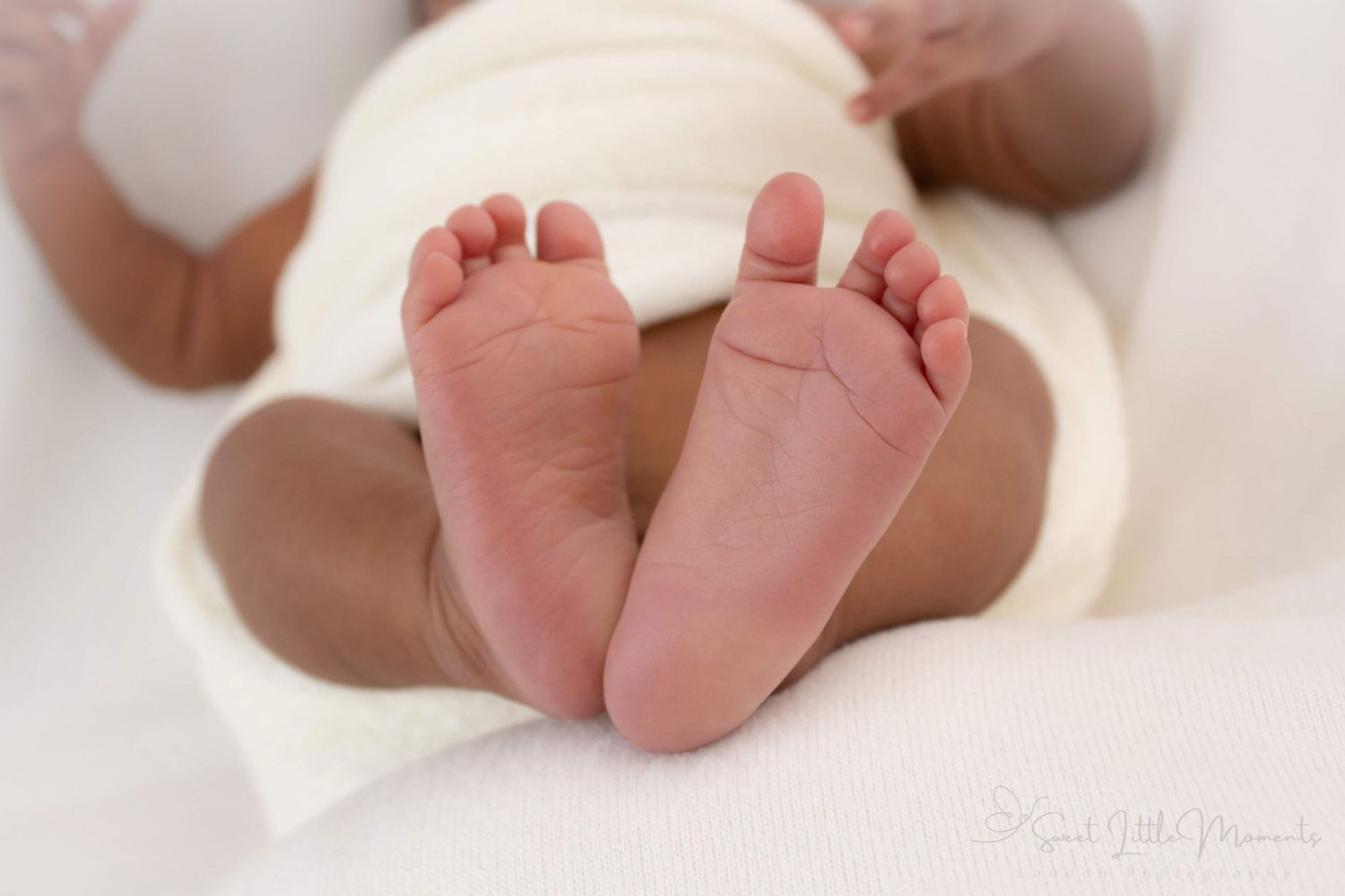 Close-up of baby feet with soft wrinkles and tiny toes against white backdrop.