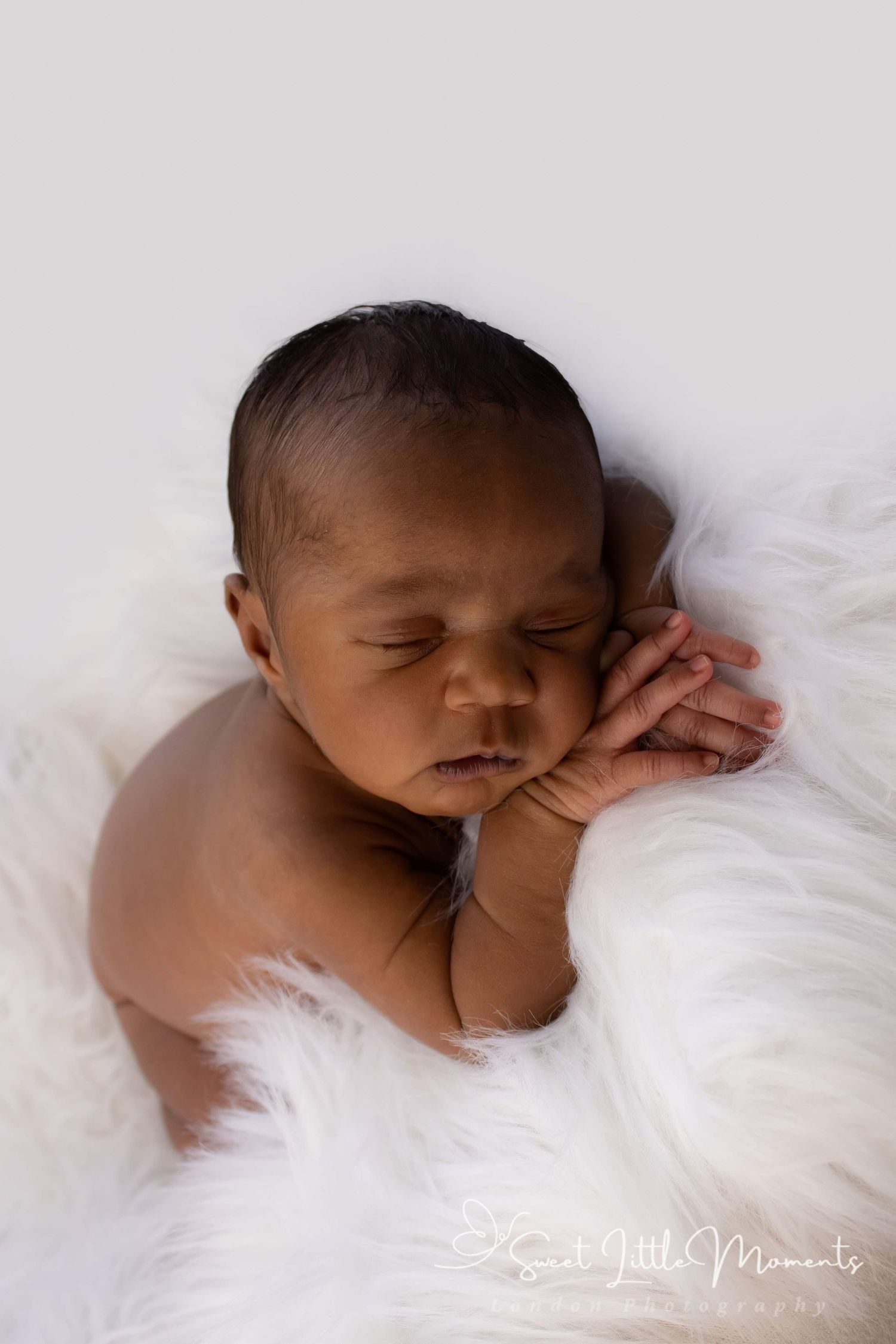 Sleeping newborn baby peacefully resting on white fur backdrop.