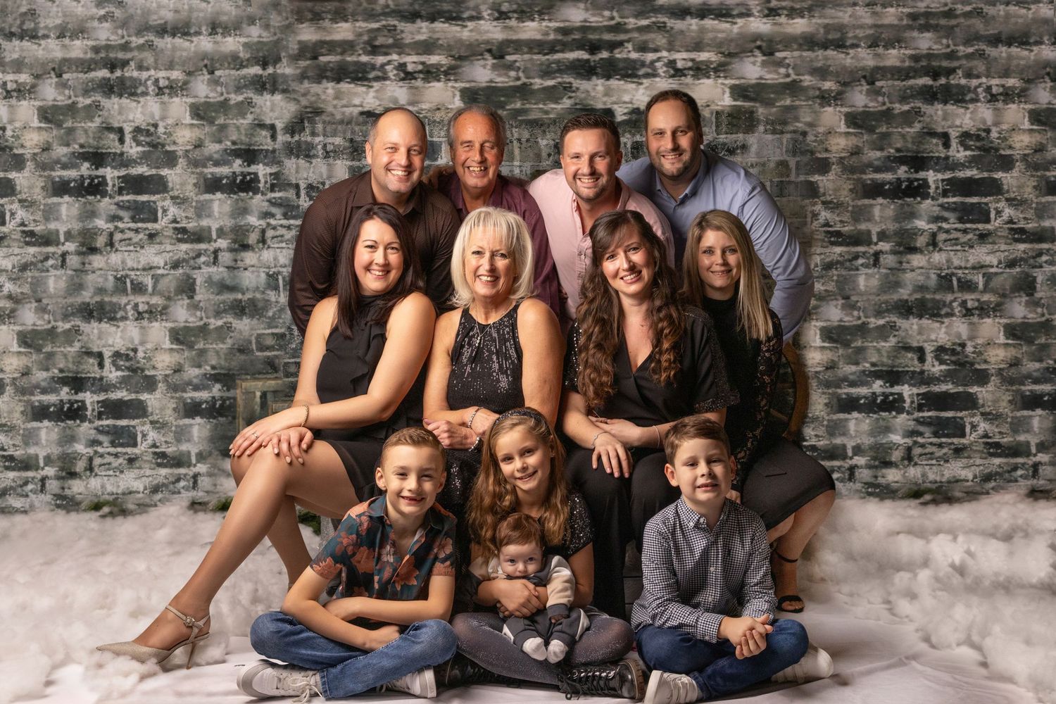 Multi-generational family portrait against textured gray wall in studio setting.