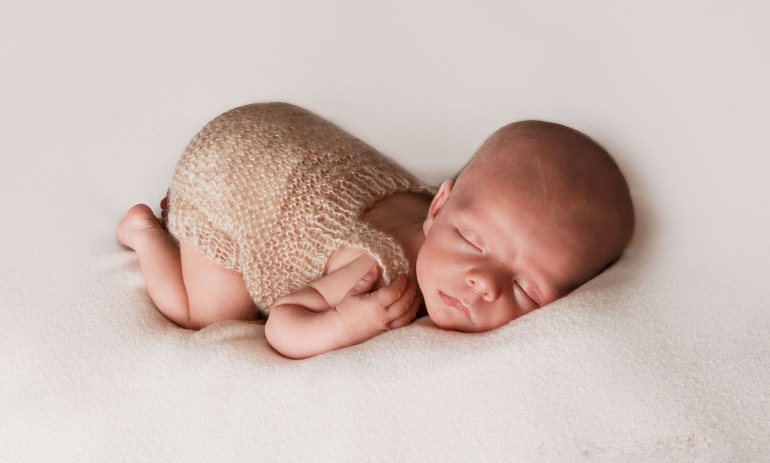 Sleeping newborn in knit wrap on cream background during studio photography session.