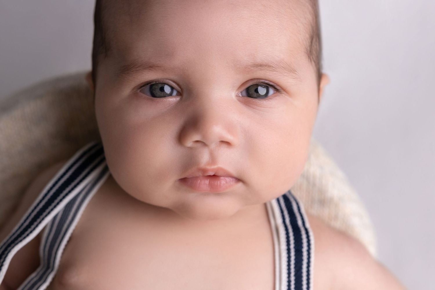 Close up portrait of baby wearing navy striped outfit against light background.