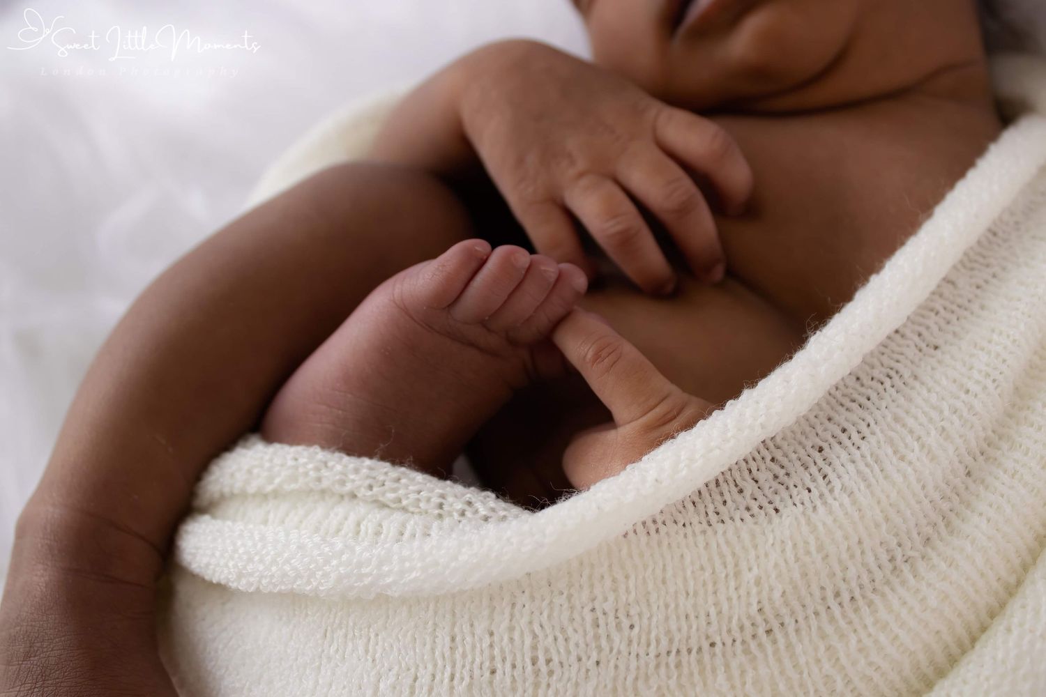 Close-up shot of tiny baby hands and feet wrapped in white cloth.