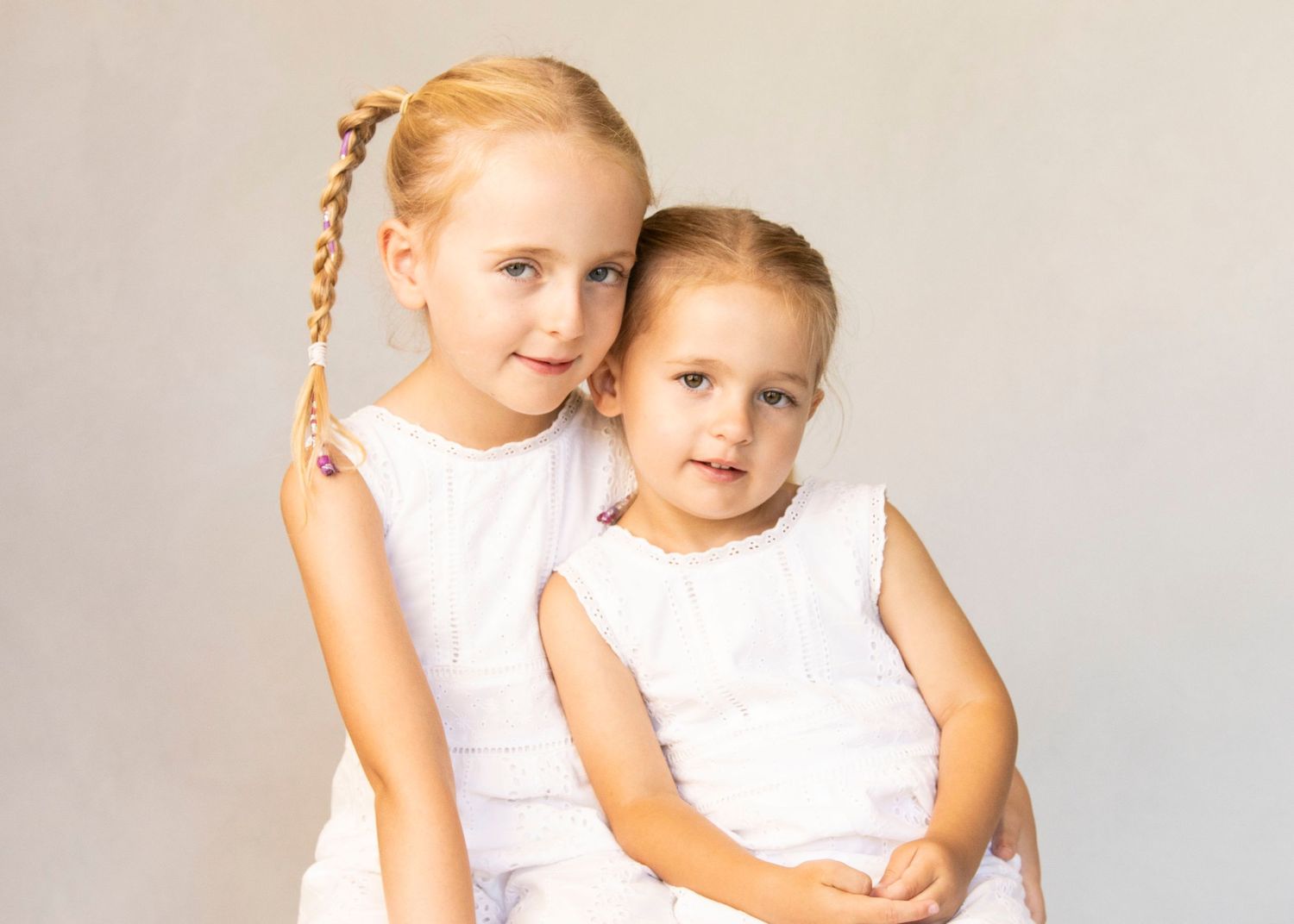 Classic studio portrait of siblings wearing matching white sleeveless dresses.