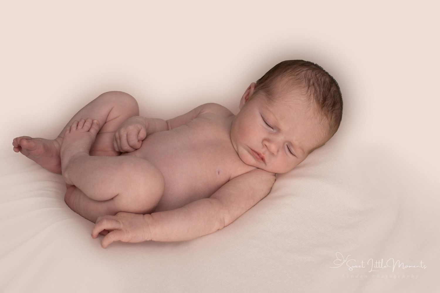 Sleeping newborn lying on side against soft beige background in artistic portrait.