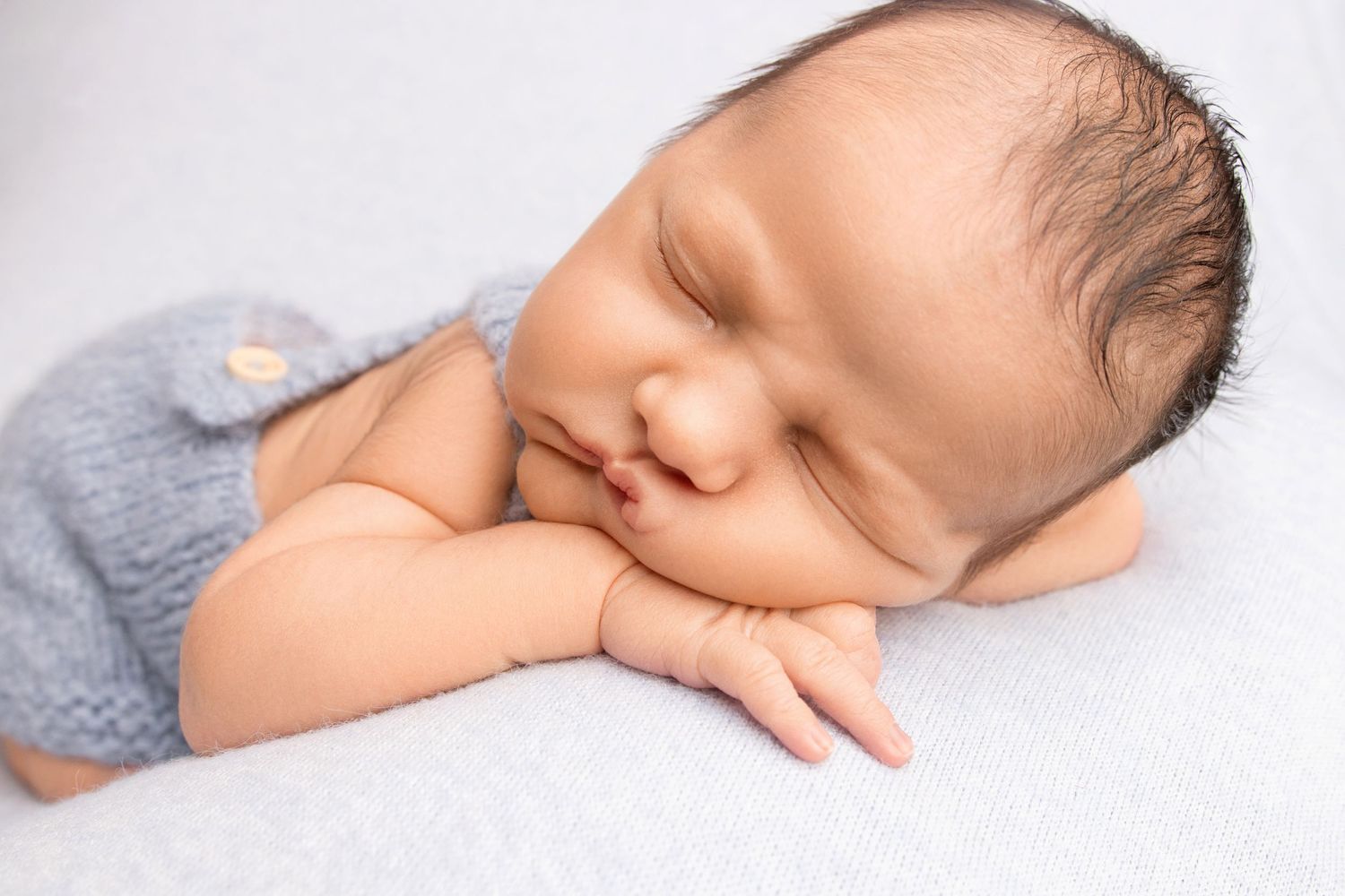 Sleeping newborn in gray knit outfit resting peacefully during portrait session.
