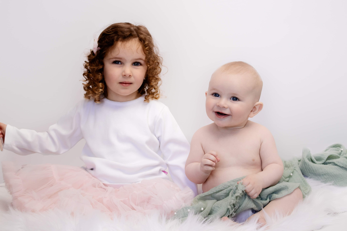 Children sitting together on white fluffy surface with pink and sage green tulle fabrics.