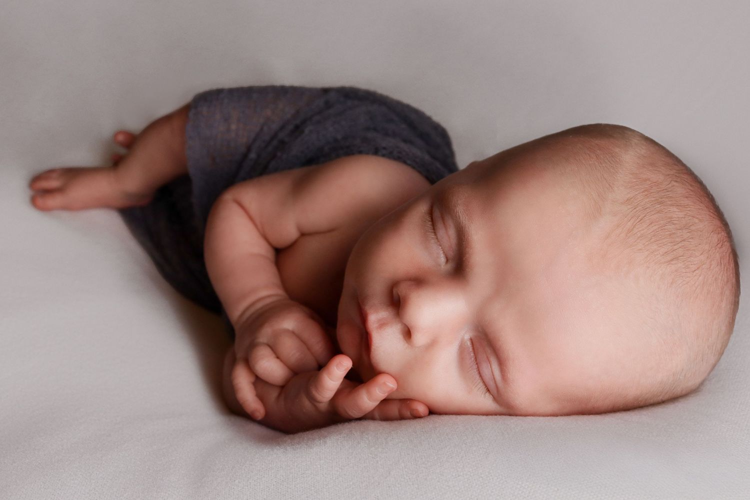 Sleeping baby in grey wrap curled up during newborn portrait session.