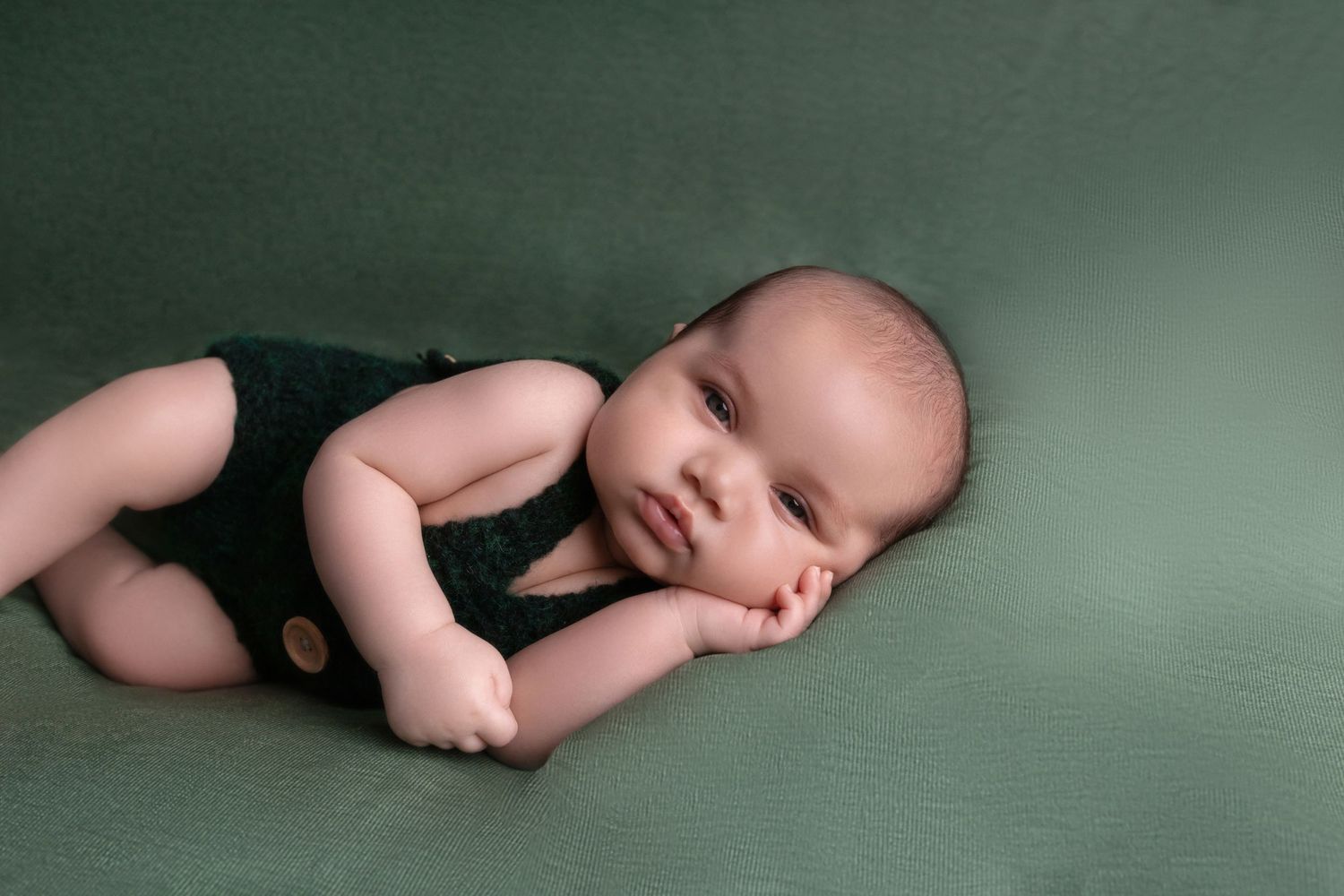 Infant in black overalls resting peacefully on green textured surface.