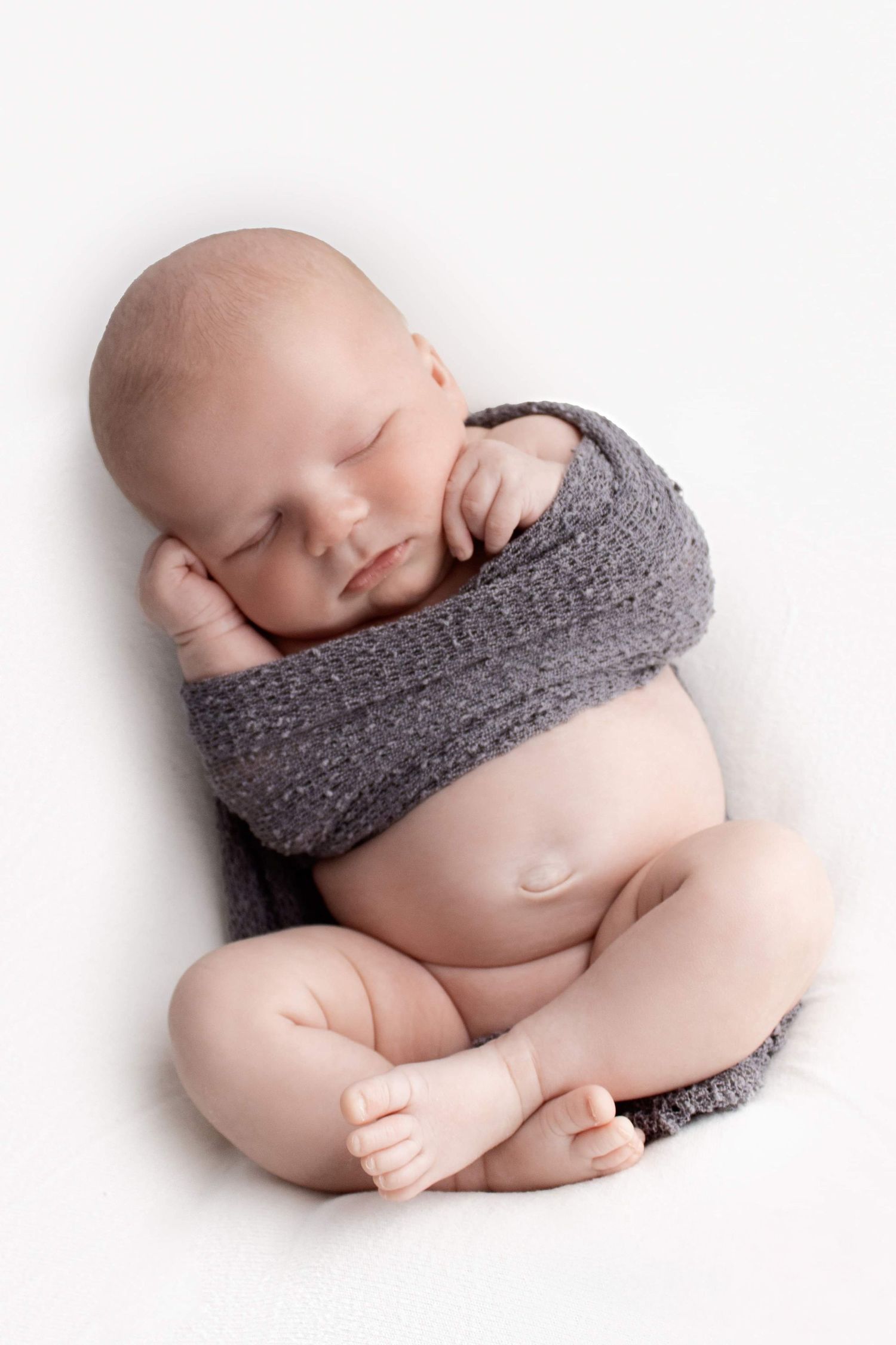 Peaceful newborn wrapped in grey knit fabric during studio portrait session.