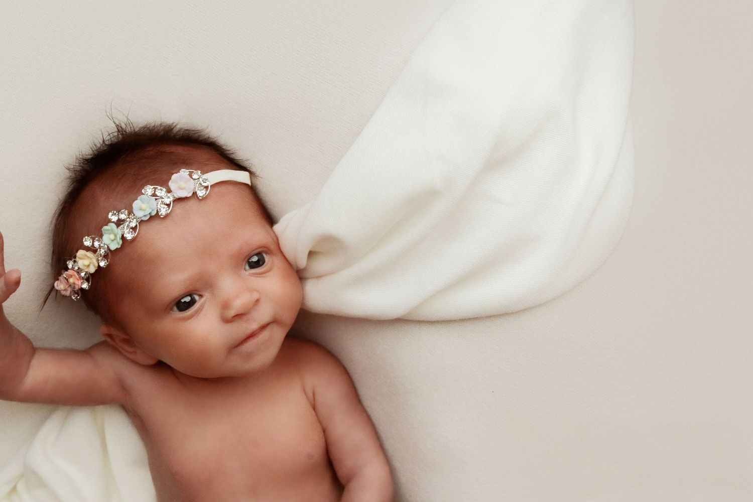 Newborn with delicate floral headband lying on soft white fabric.