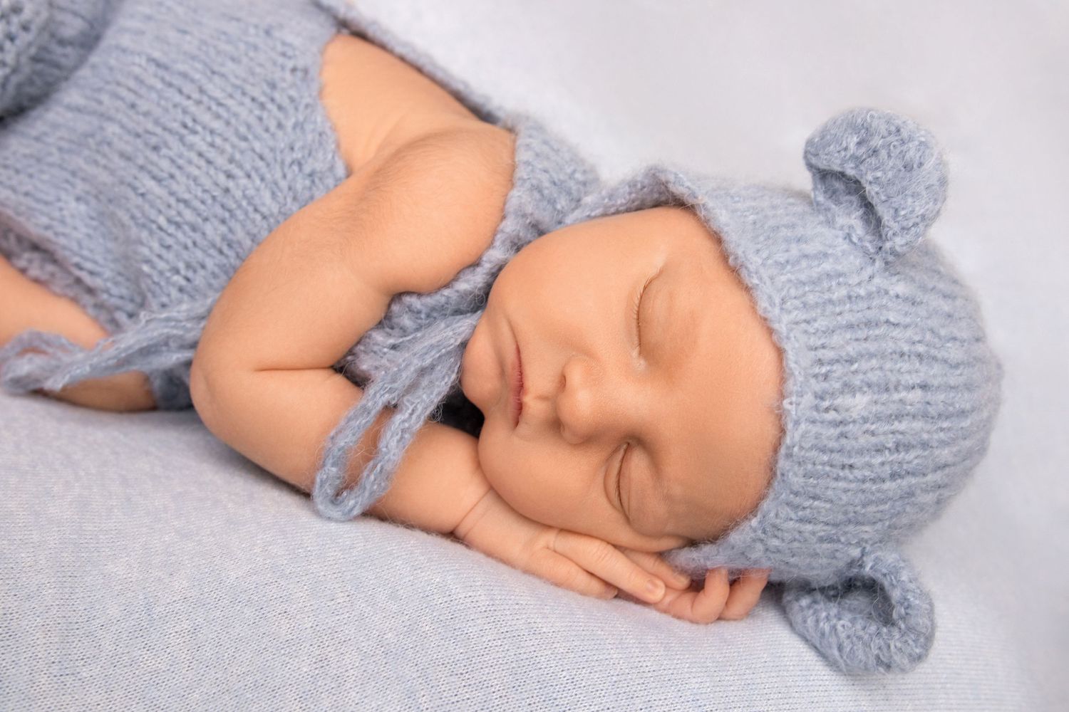 Sleeping baby wearing knitted gray hat and wrap during professional portrait session.