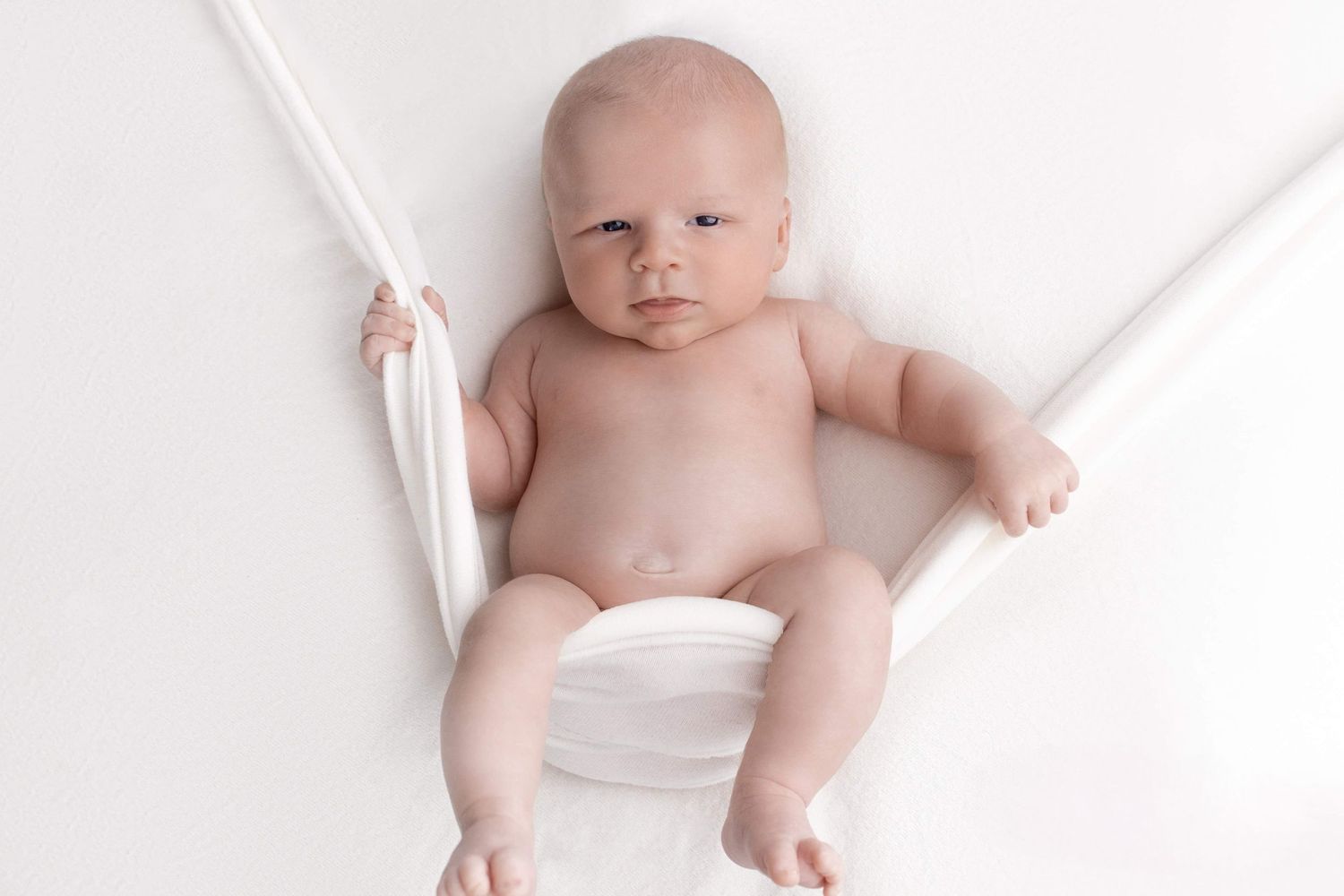 Baby lying on white fabric during minimalist studio photography session.
