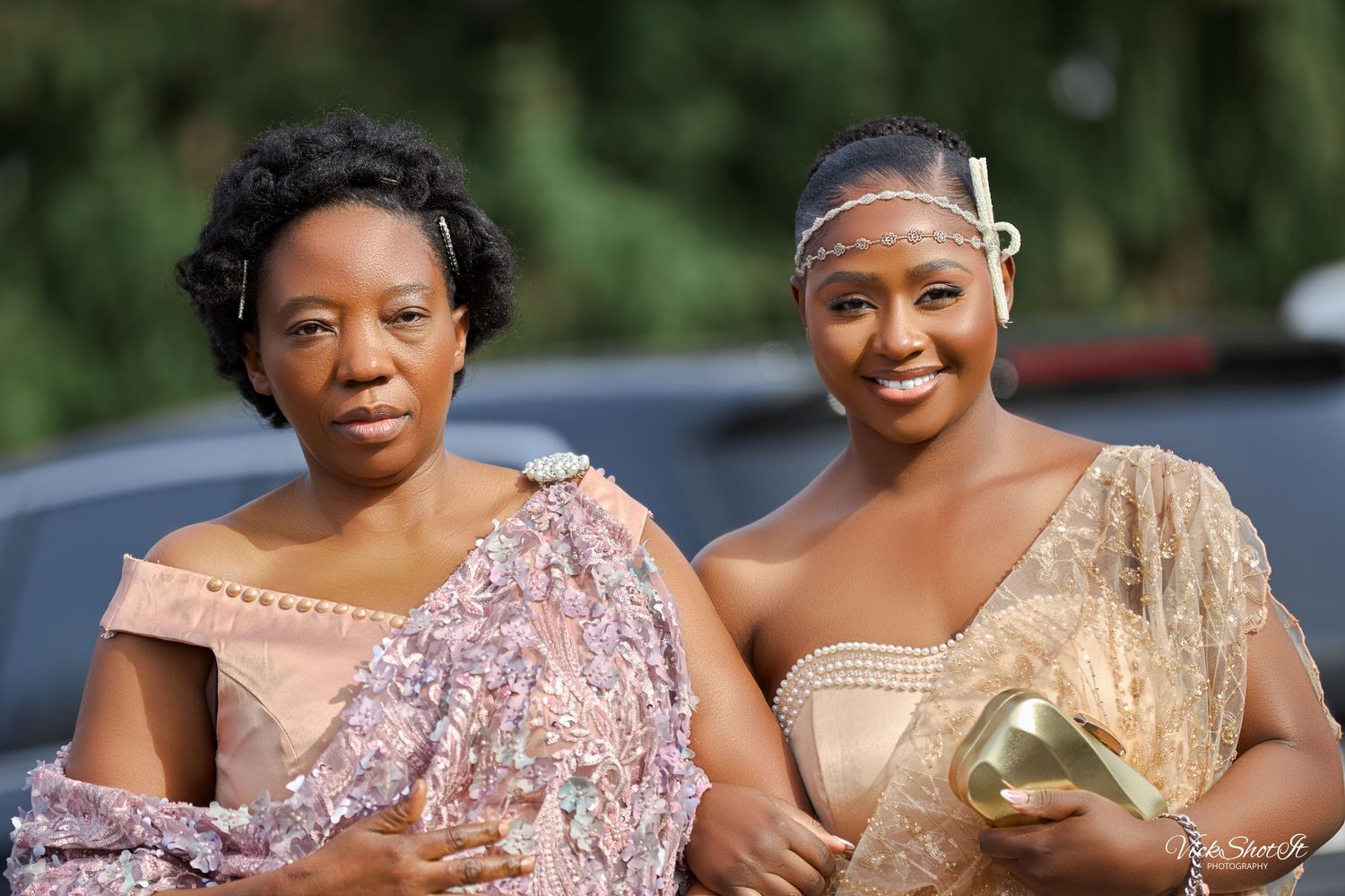 Two women in elegant formal dresses share a happy moment outdoors.